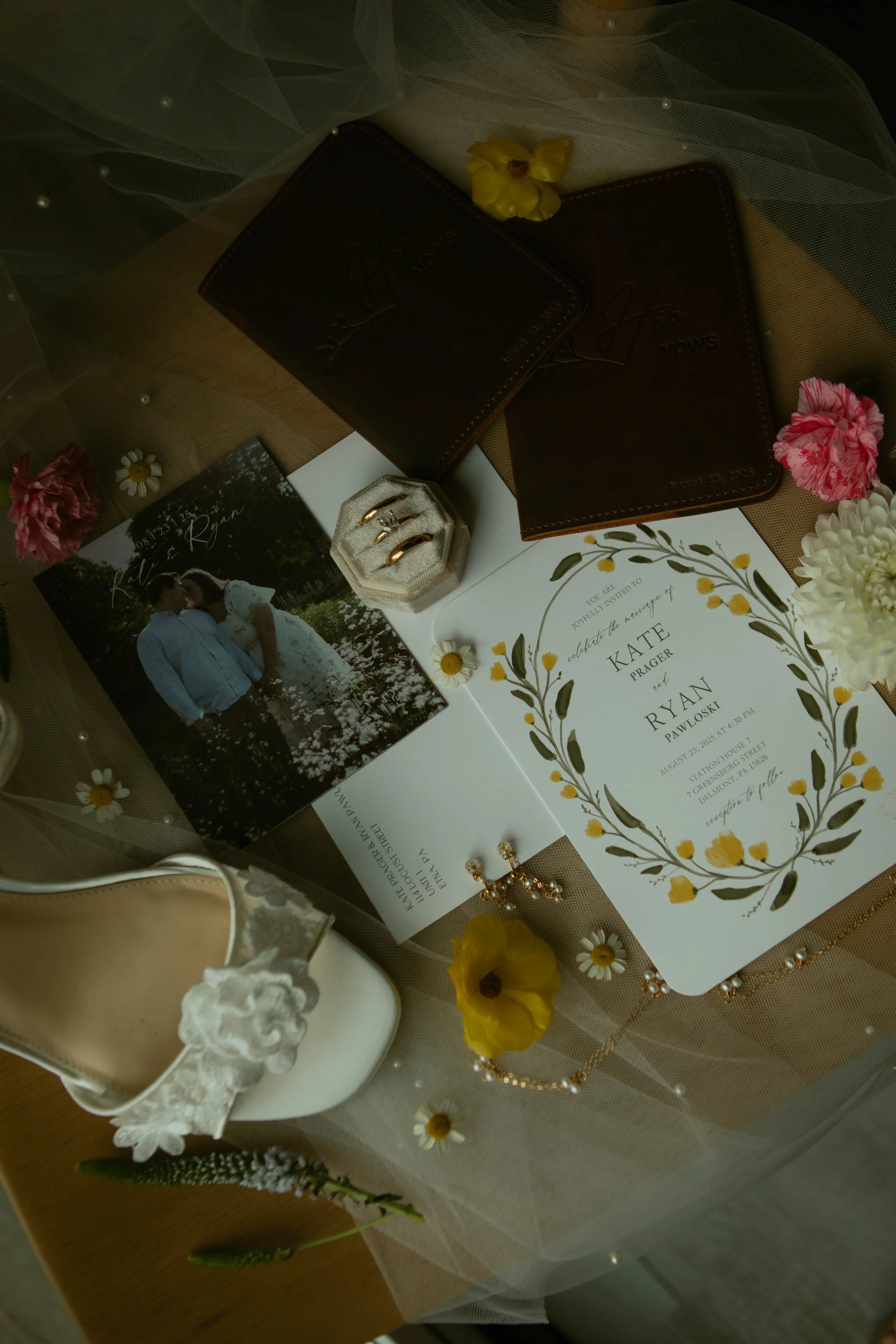 Wedding invitation surrounded by wedding accessories such as a ring box, shoes, a necklace, earrings, a wedding photo, and flowers.