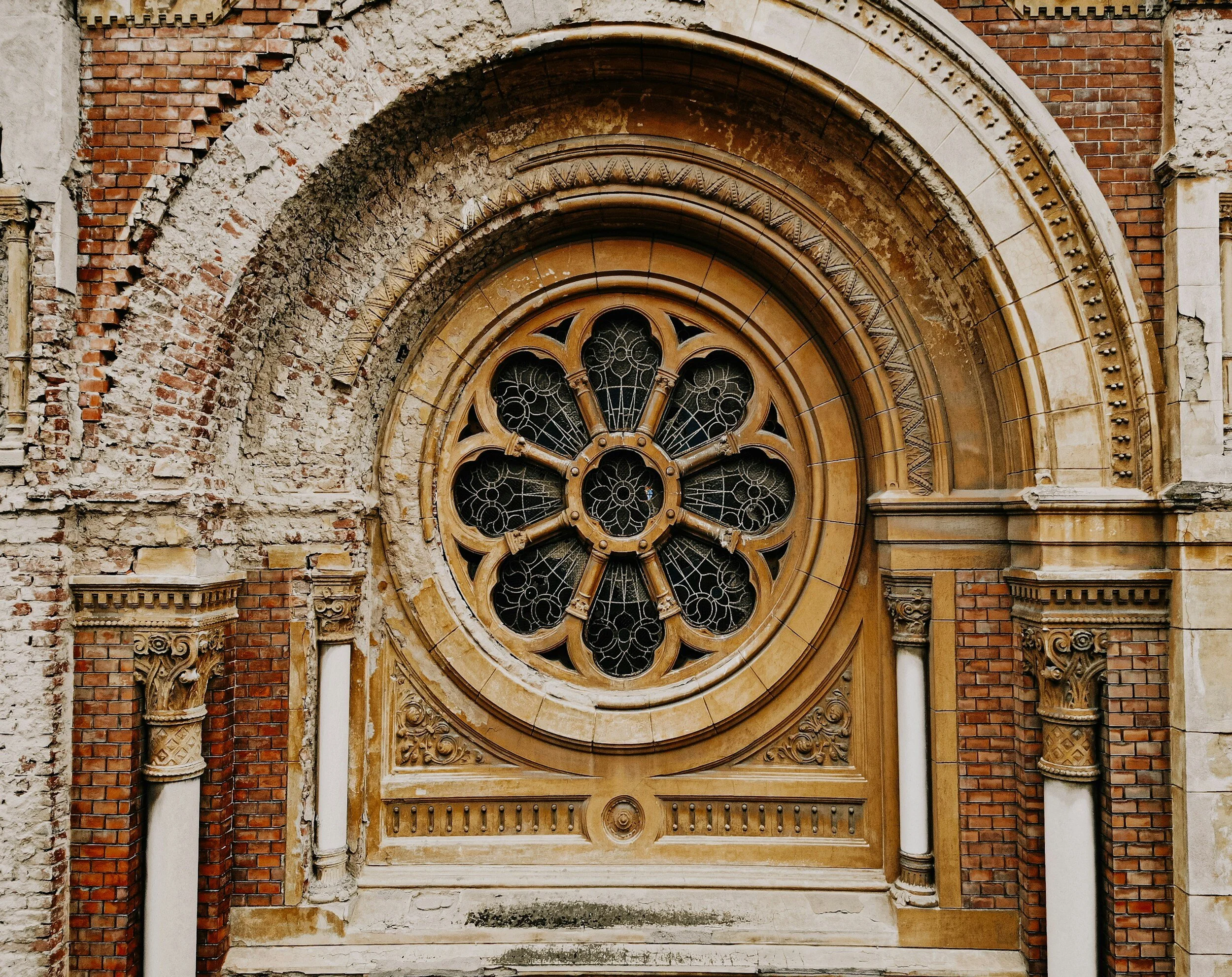 Close-up of a historic building's arched stone and brick facade with a large circular stained glass window surrounded by ornate architectural details.