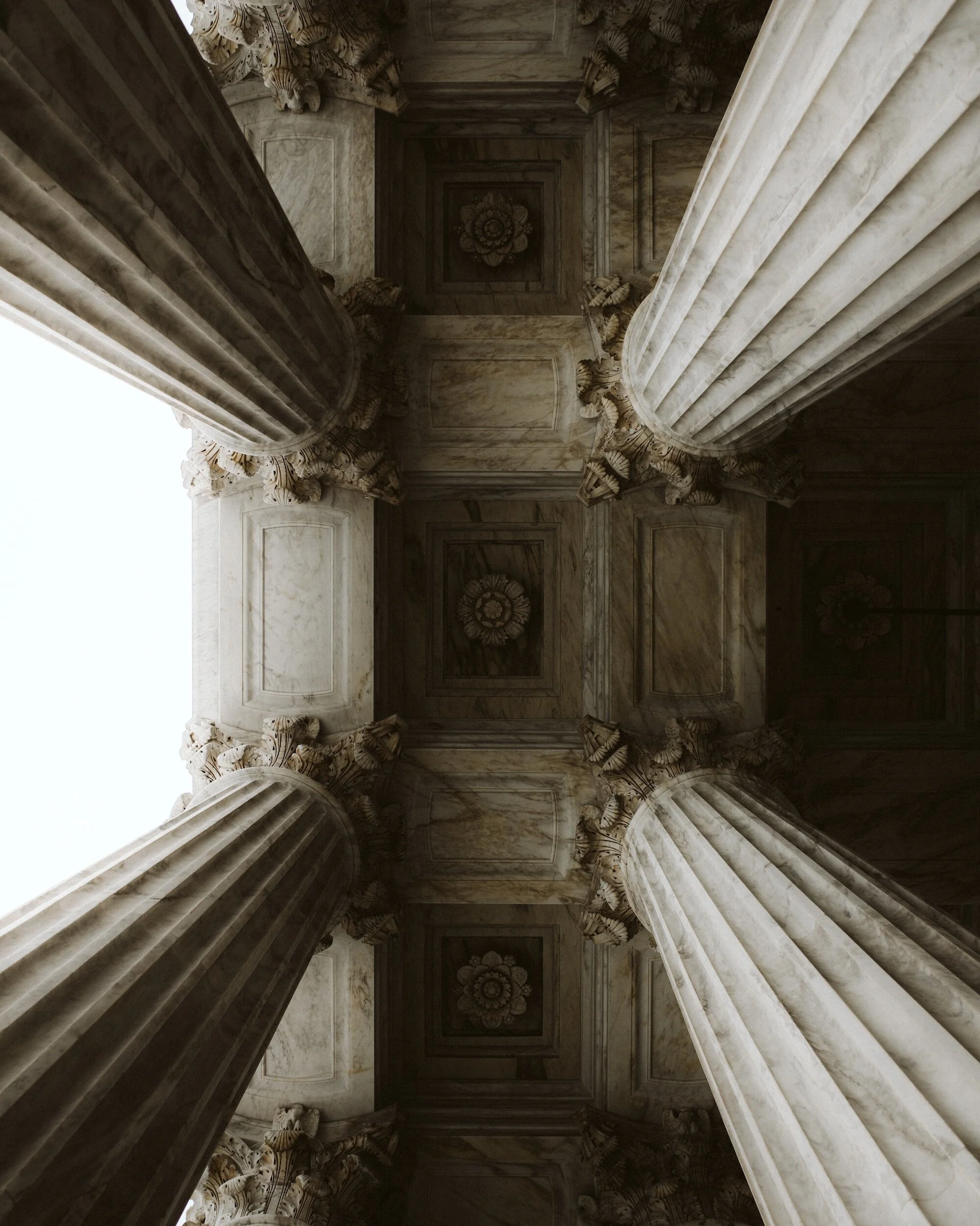 Looking up at marble columns supporting a decorated ceiling in a grand historic building.
