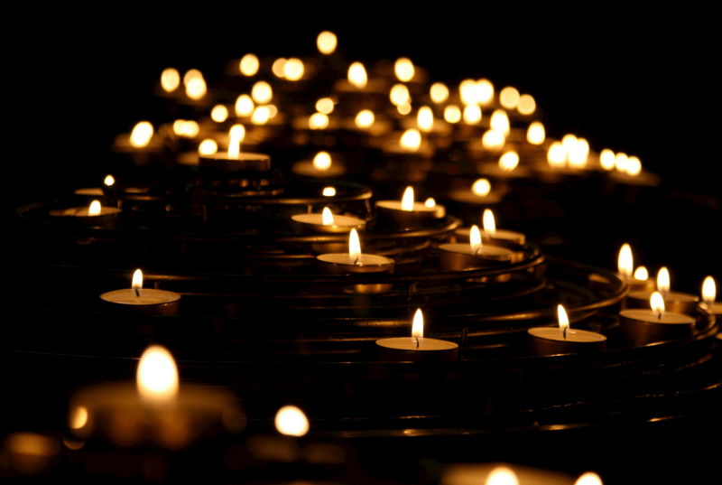 Multiple small candles placed on a surface with some arranged in a spiral pattern, glowing softly in darkness, creating a warm and tranquil ambiance.