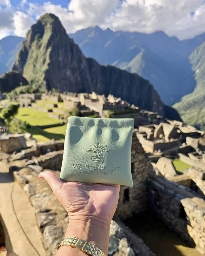 A person holding a green packet labeled 'My Prayer Kit' with Machu Picchu in the background, surrounded by mountains and ancient ruins.