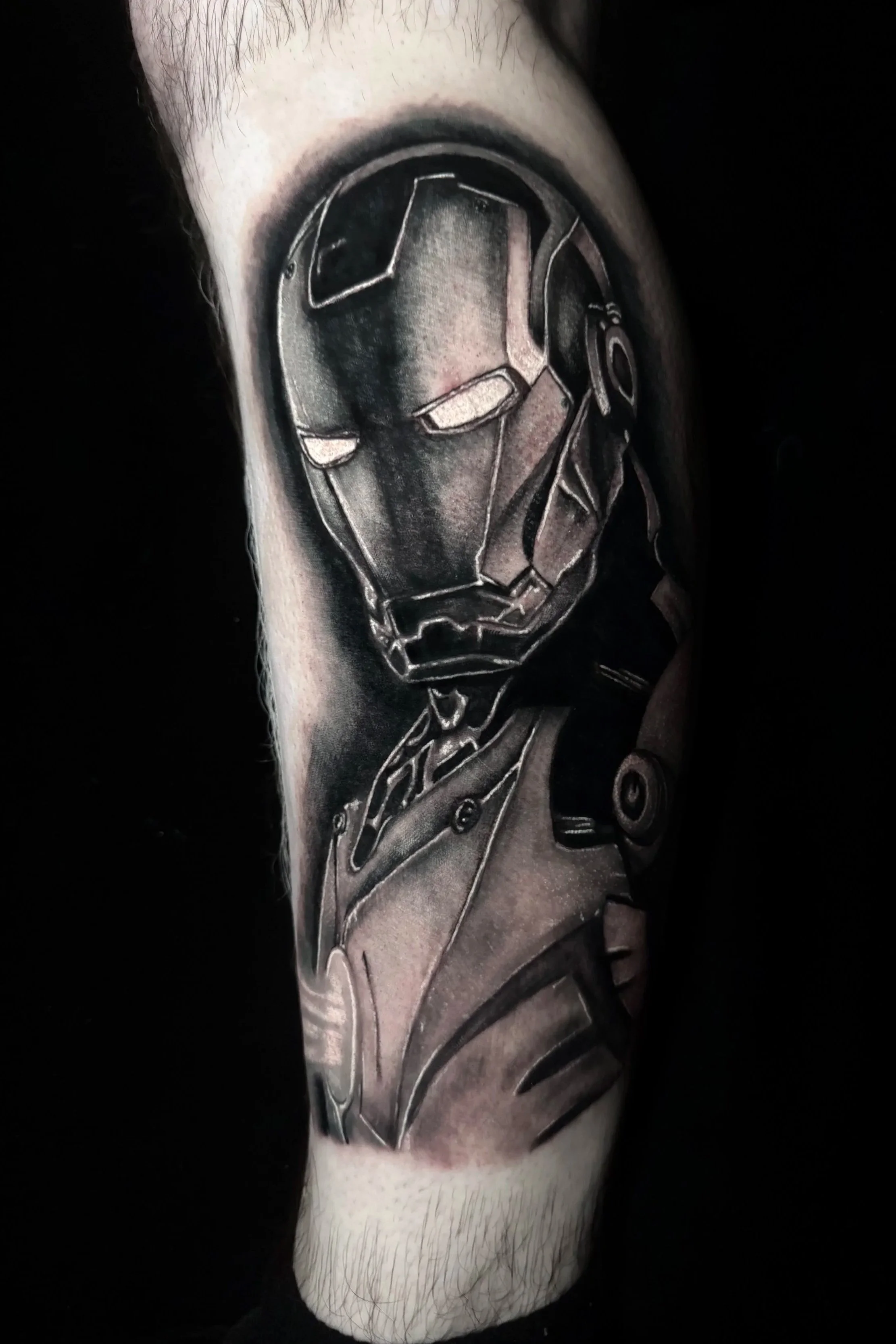 Black and gray replica tattoo of Iron Man's helmet on individual's upper arm.