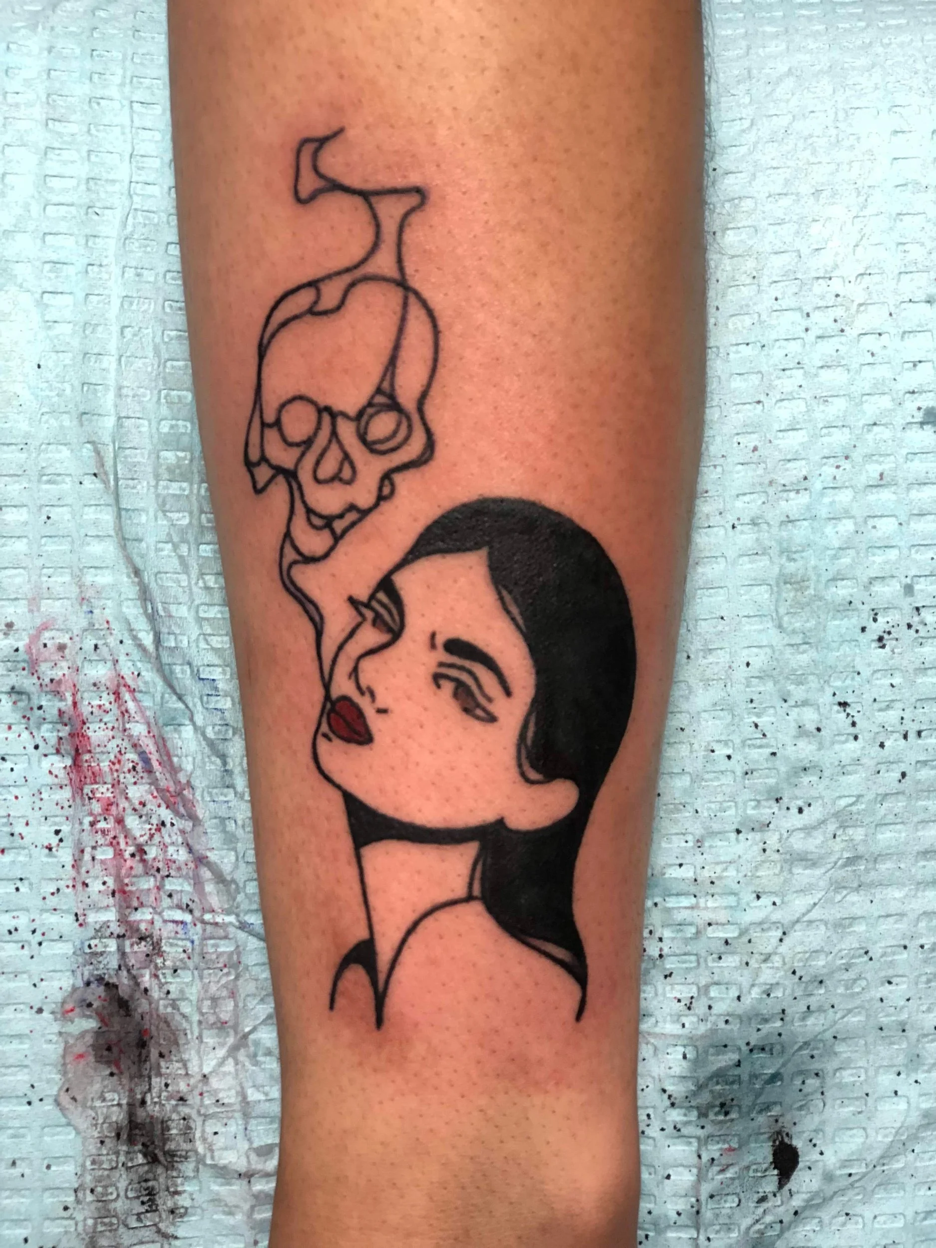 Tattoo of a woman's face with dark hair and red lips, smoke rising from her mouth, on person's arm.