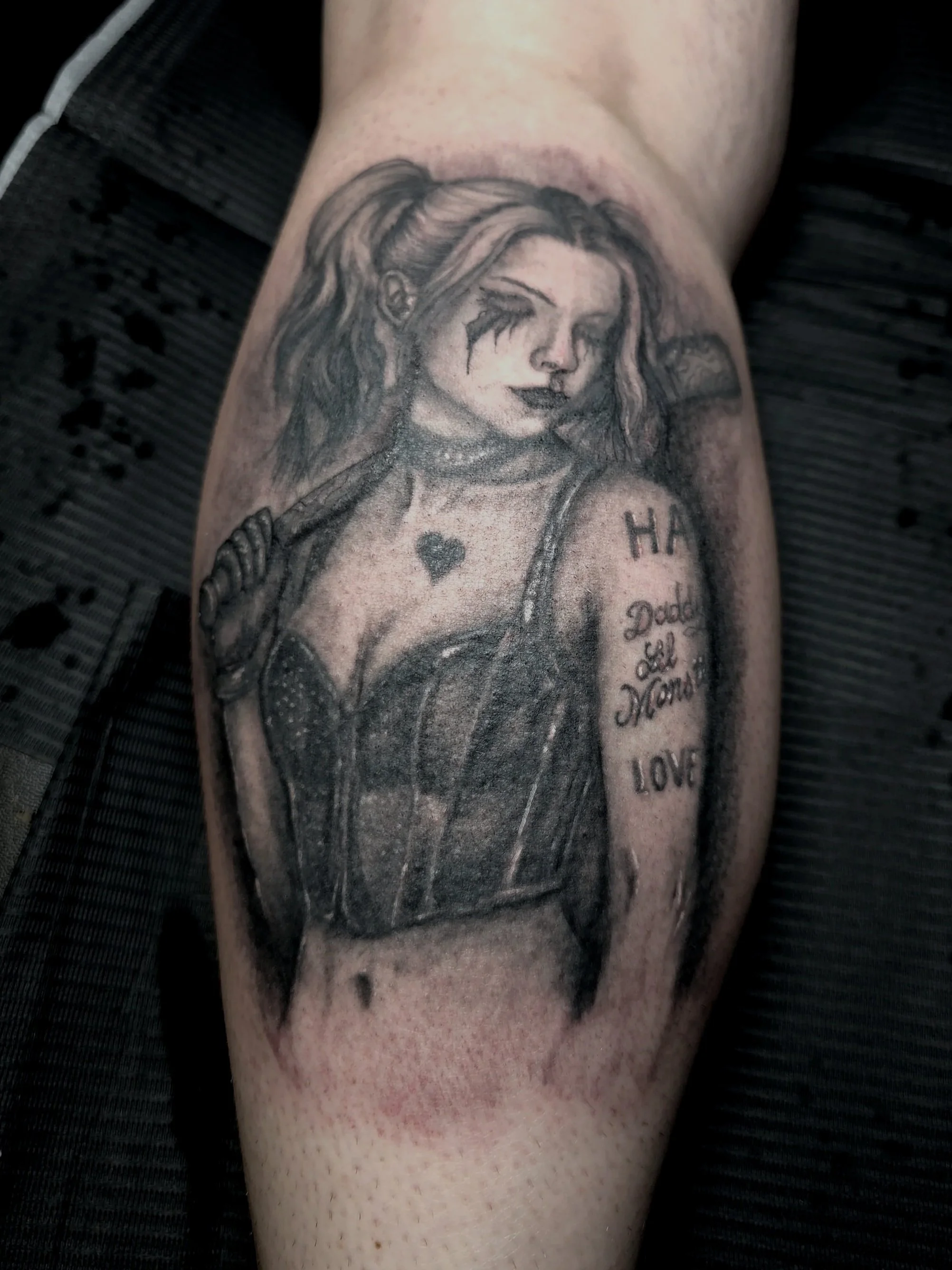 Black and gray tattoo of a woman with long hair and tears on her face, holding a gun, with words tattooed on her arm.