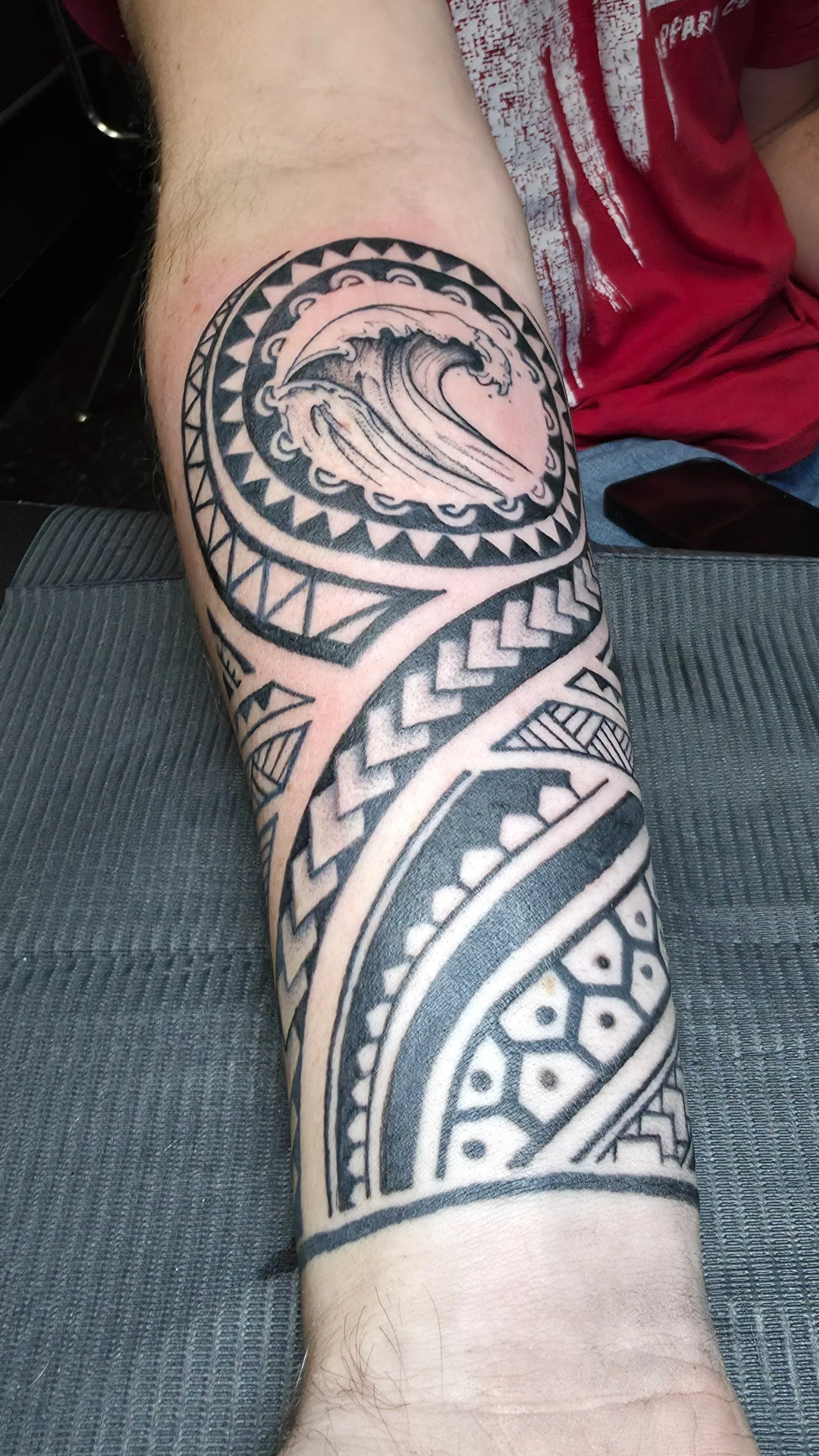 Tattoo sleeve on person's arm featuring Polynesian-style patterns and a large wave design.