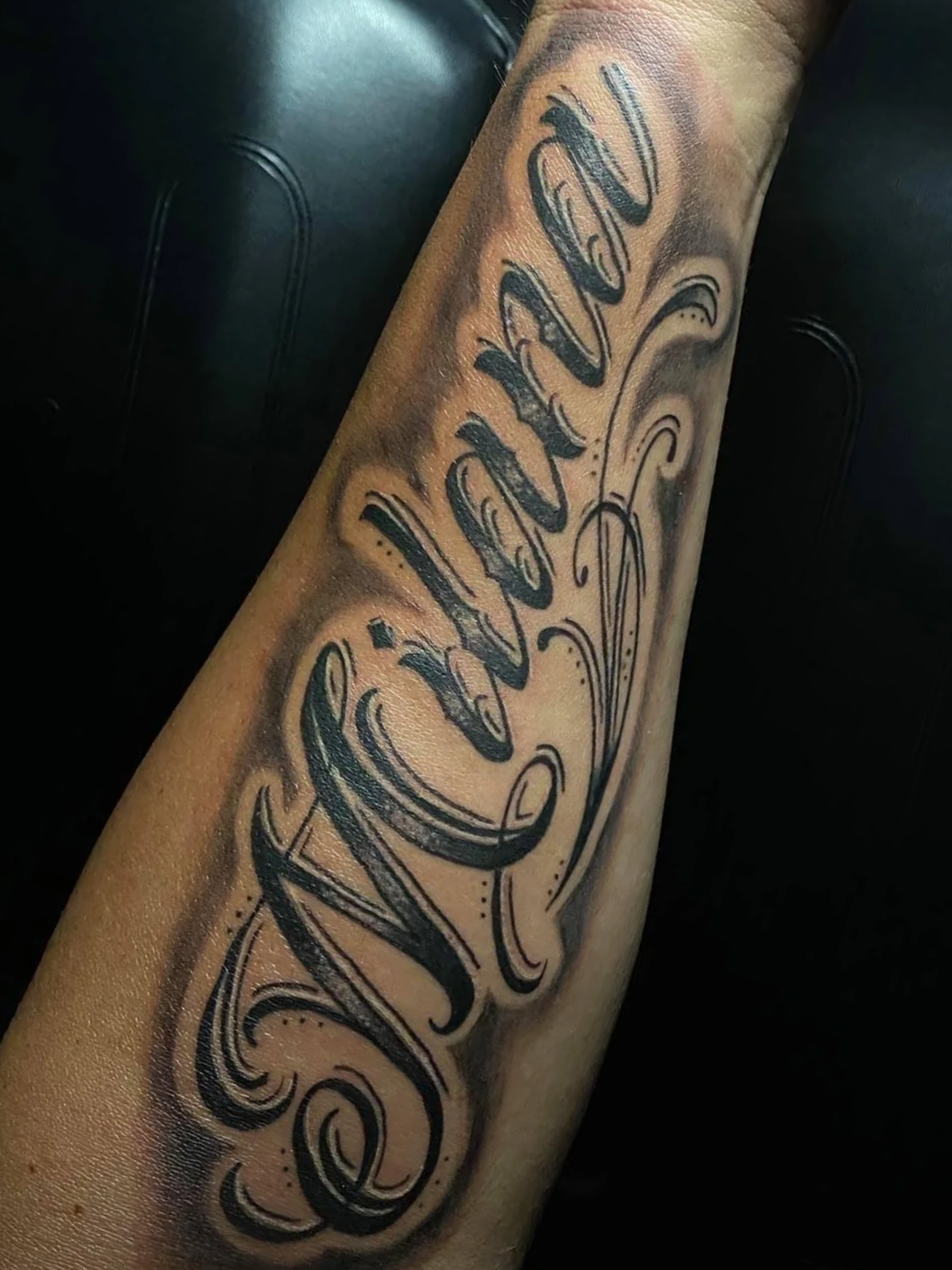 Tattoo on person's arm with swirling script that says "Shawn" in black ink with decorative shading.