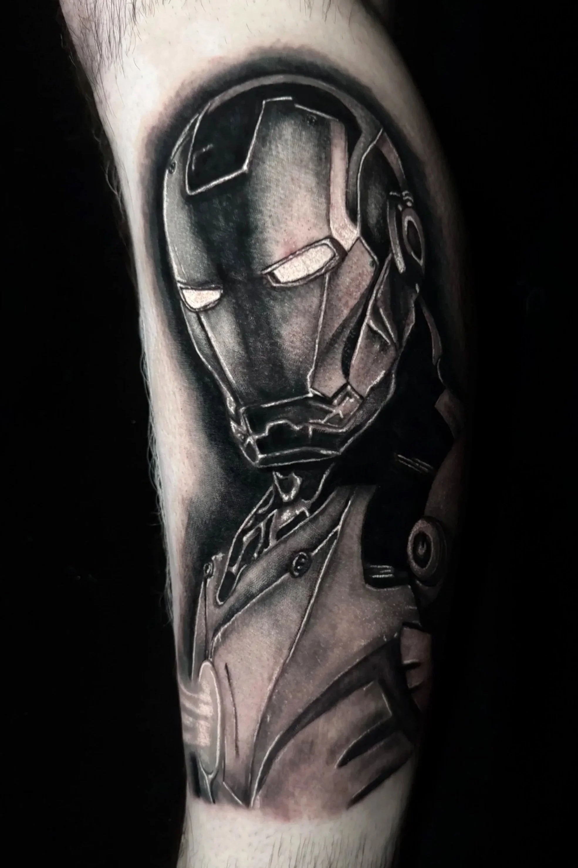 Black and gray tattoo of a mask with mechanical details on a person's upper arm.