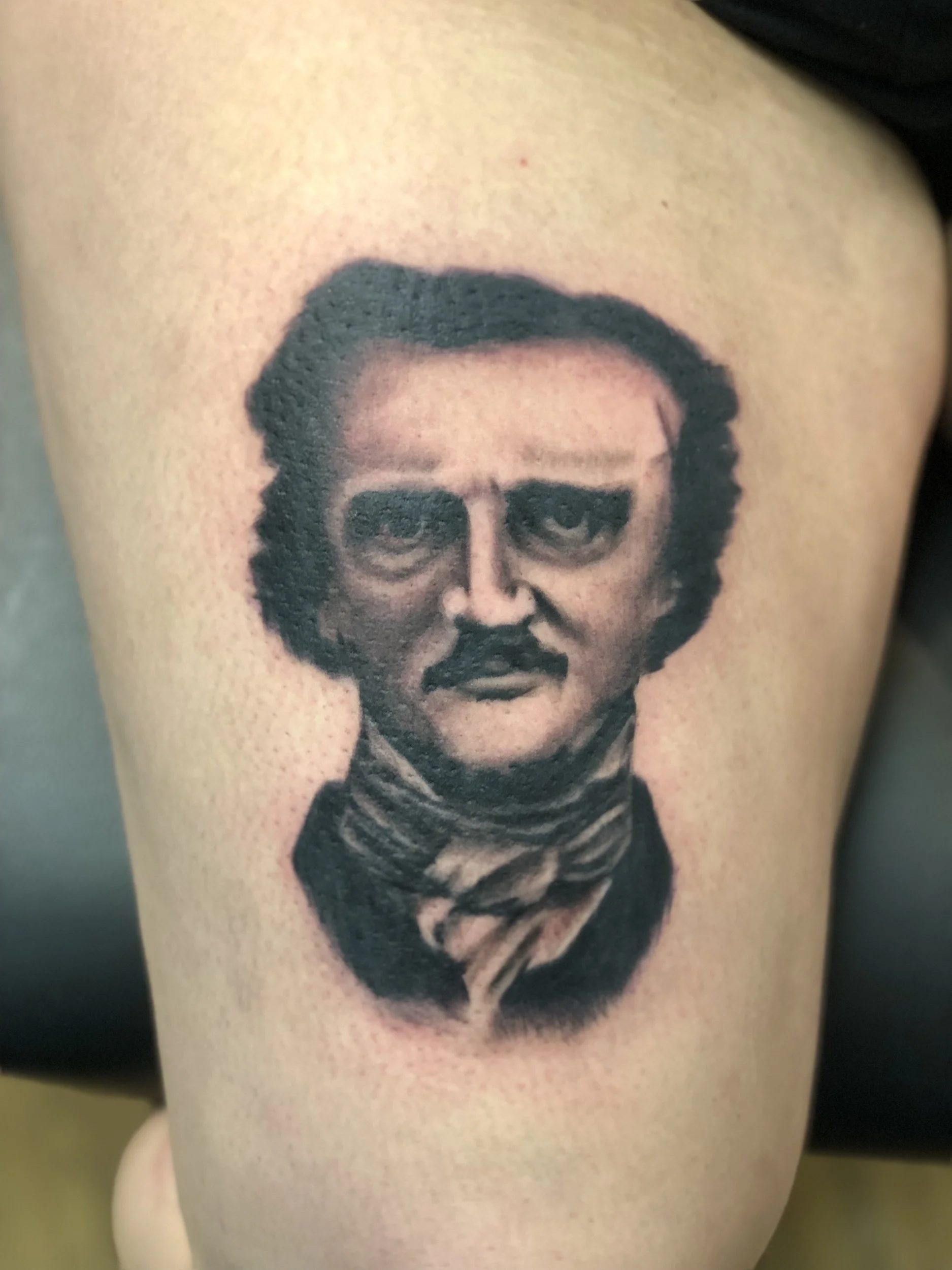 Close-up of a tattoo of a man's face with glasses and a beard on a person's arm.