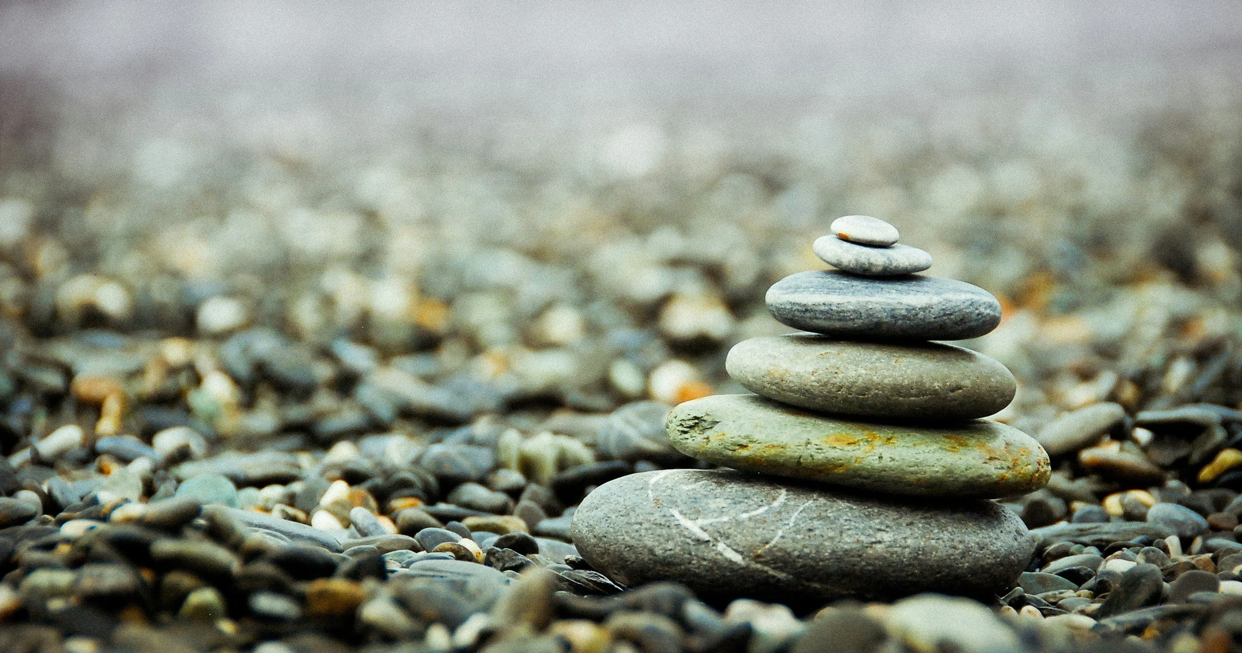 Stack of five smooth gray stones balanced on a bed of small pebbles with a blurred background.