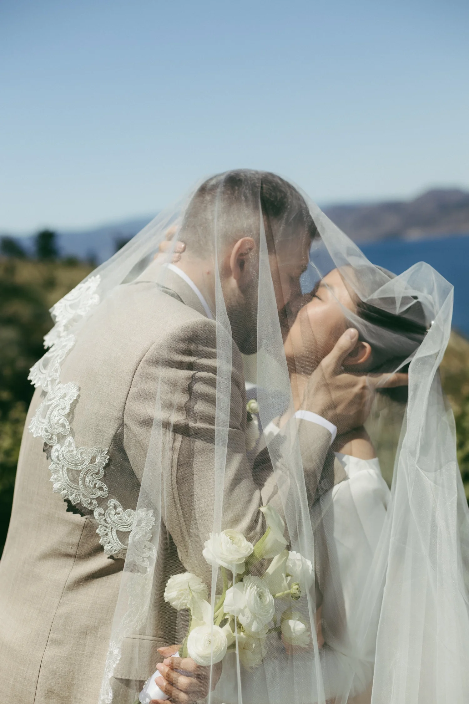 A bride and groom kissing beneath her veil, sunlight coming through the fabric
