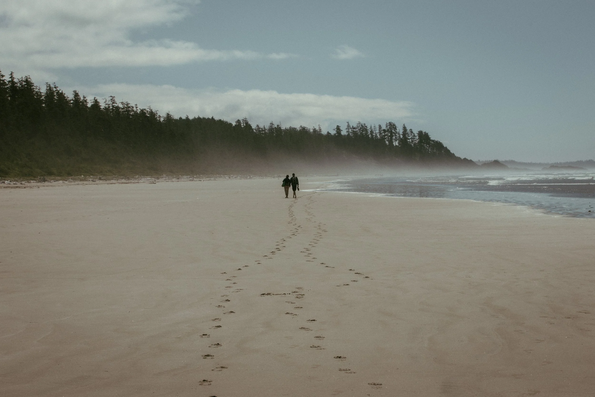 A couple walking a wide, misty beach at low tide, small against the shoreline