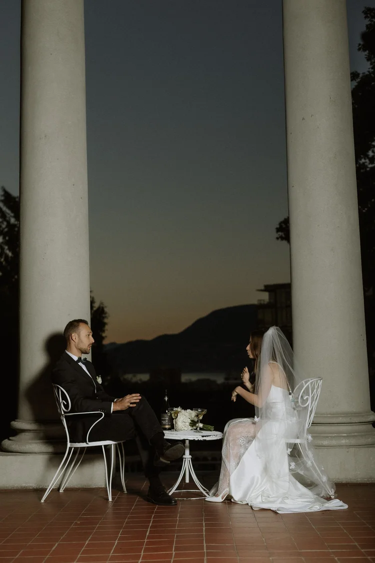 A bride and groom seated between stone columns at blue hour