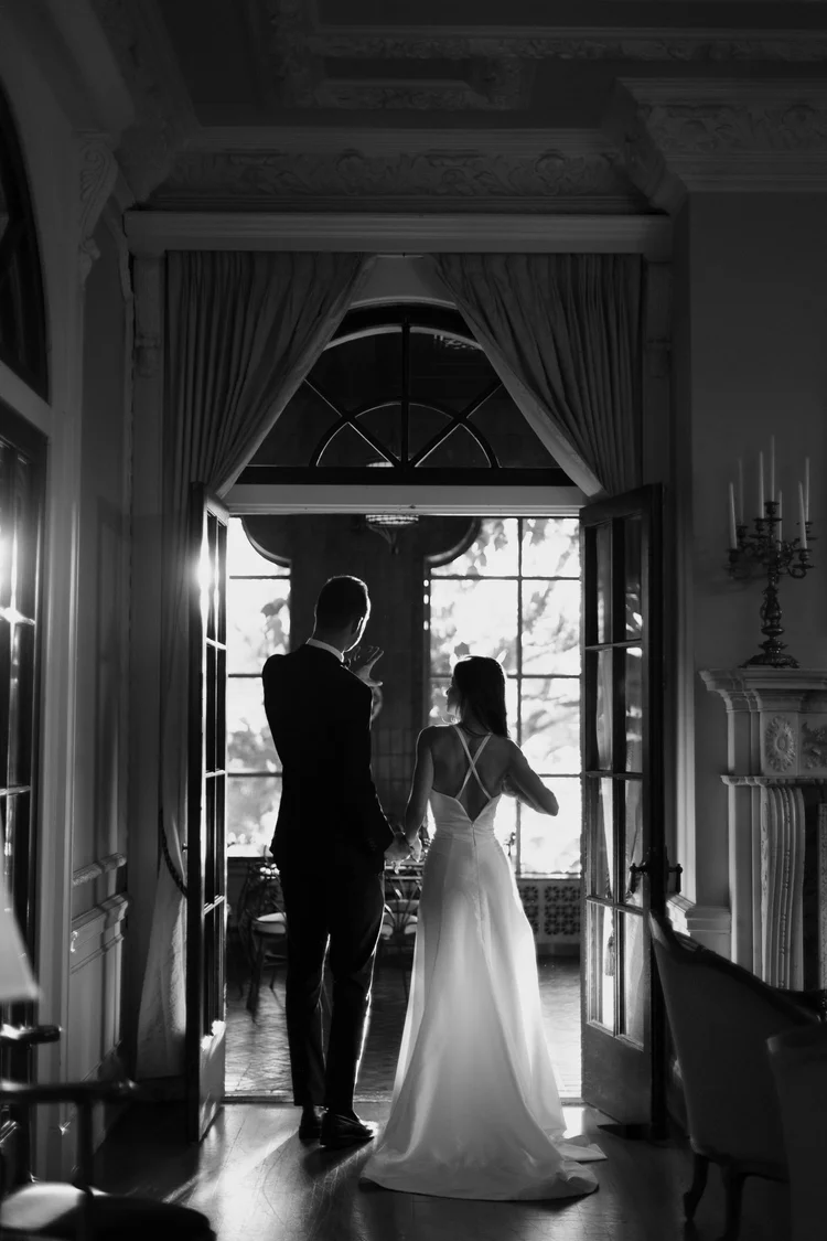 Black and white photograph of a bride and groom framed in a tall doorway at Hycroft Manor