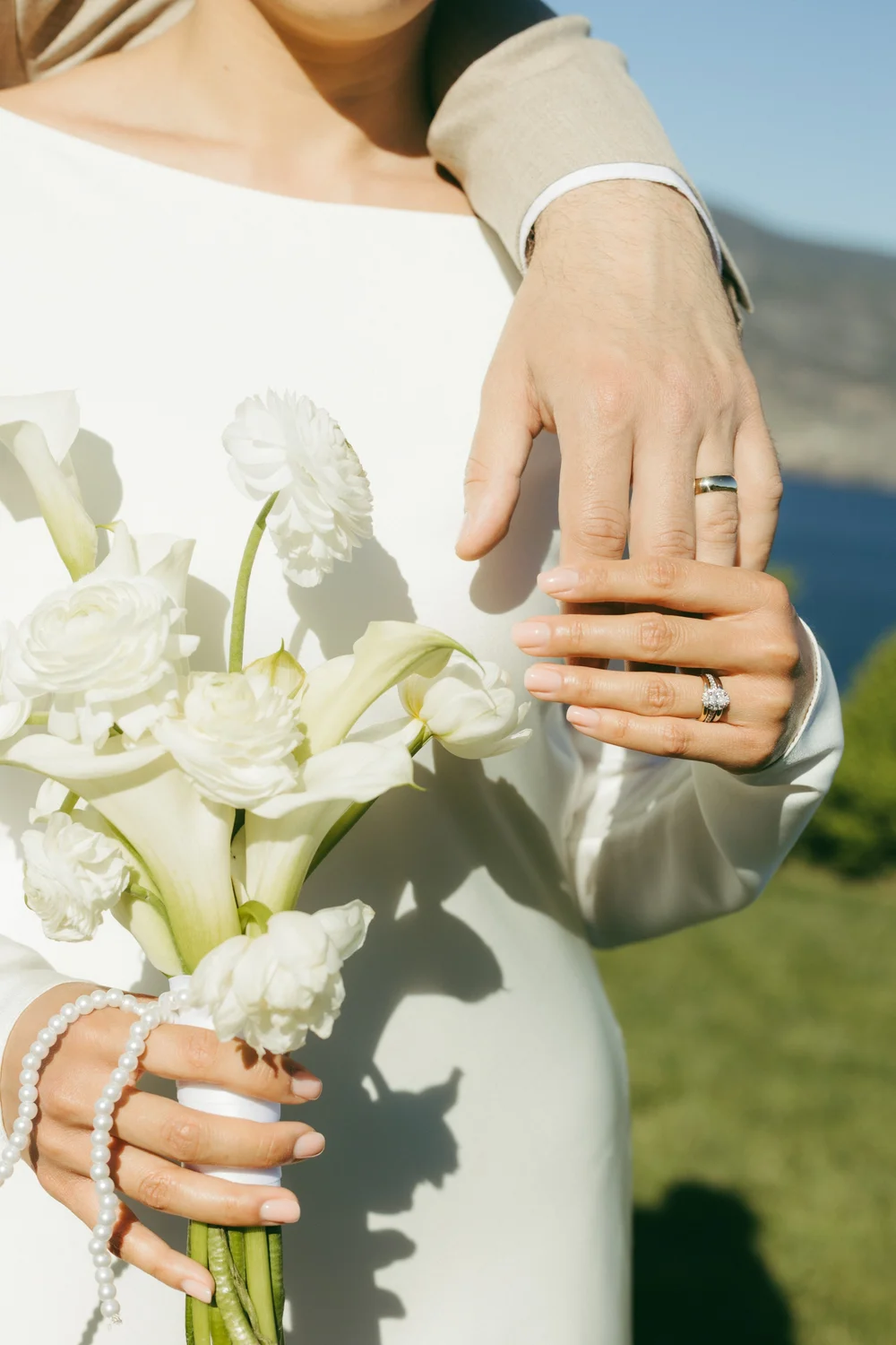 Close detail of a bride's hand and wedding ring resting on a bouquet of white calla lilies