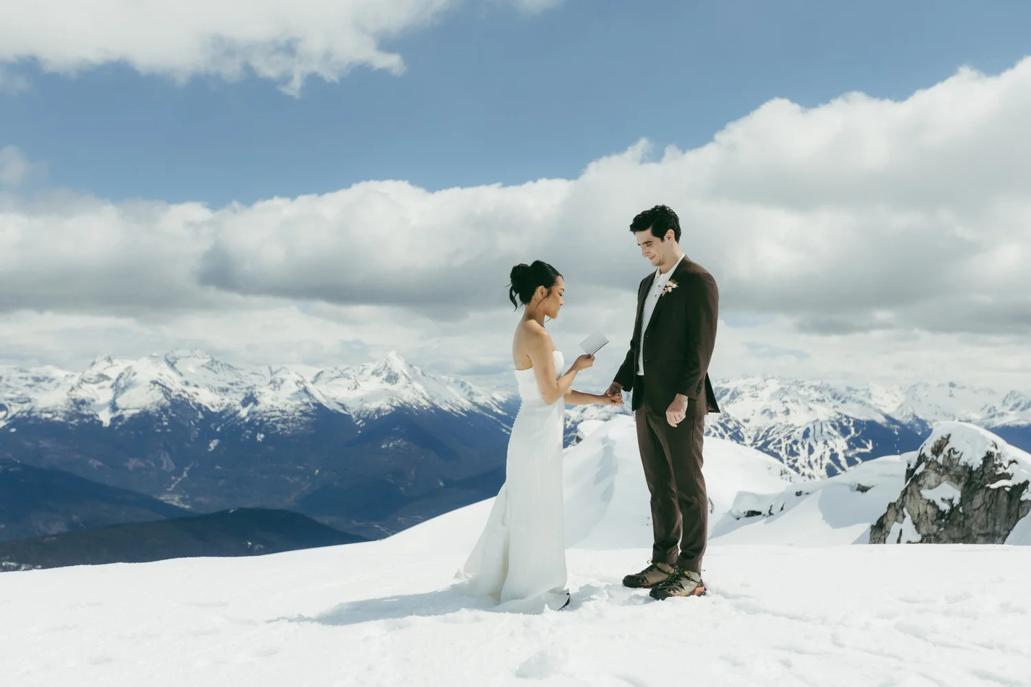 A bride and groom on a snowy summit above a sweeping range of mountains