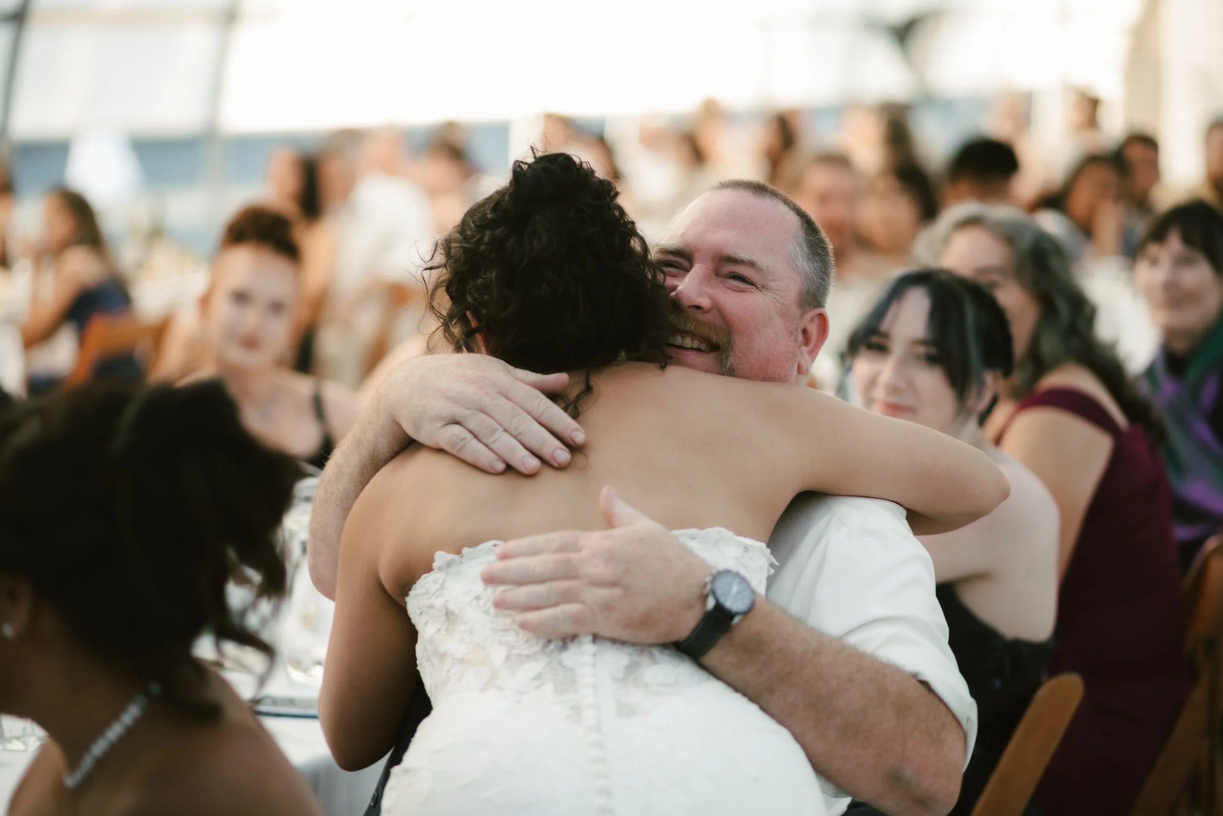 Newlywed couple embracing and smiling at their wedding reception surrounded by guests