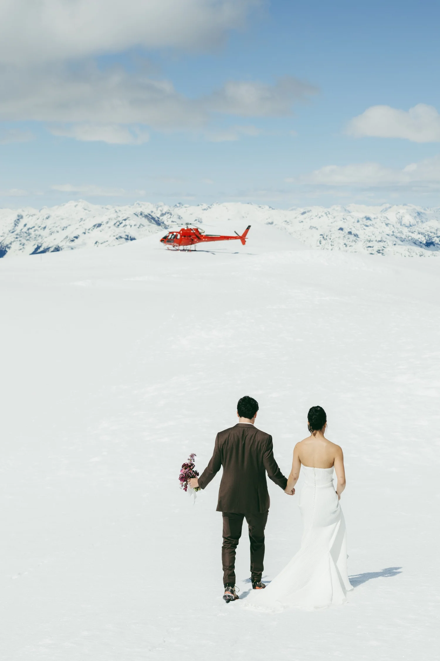 A bride and groom walking across a snowfield toward a waiting helicopter