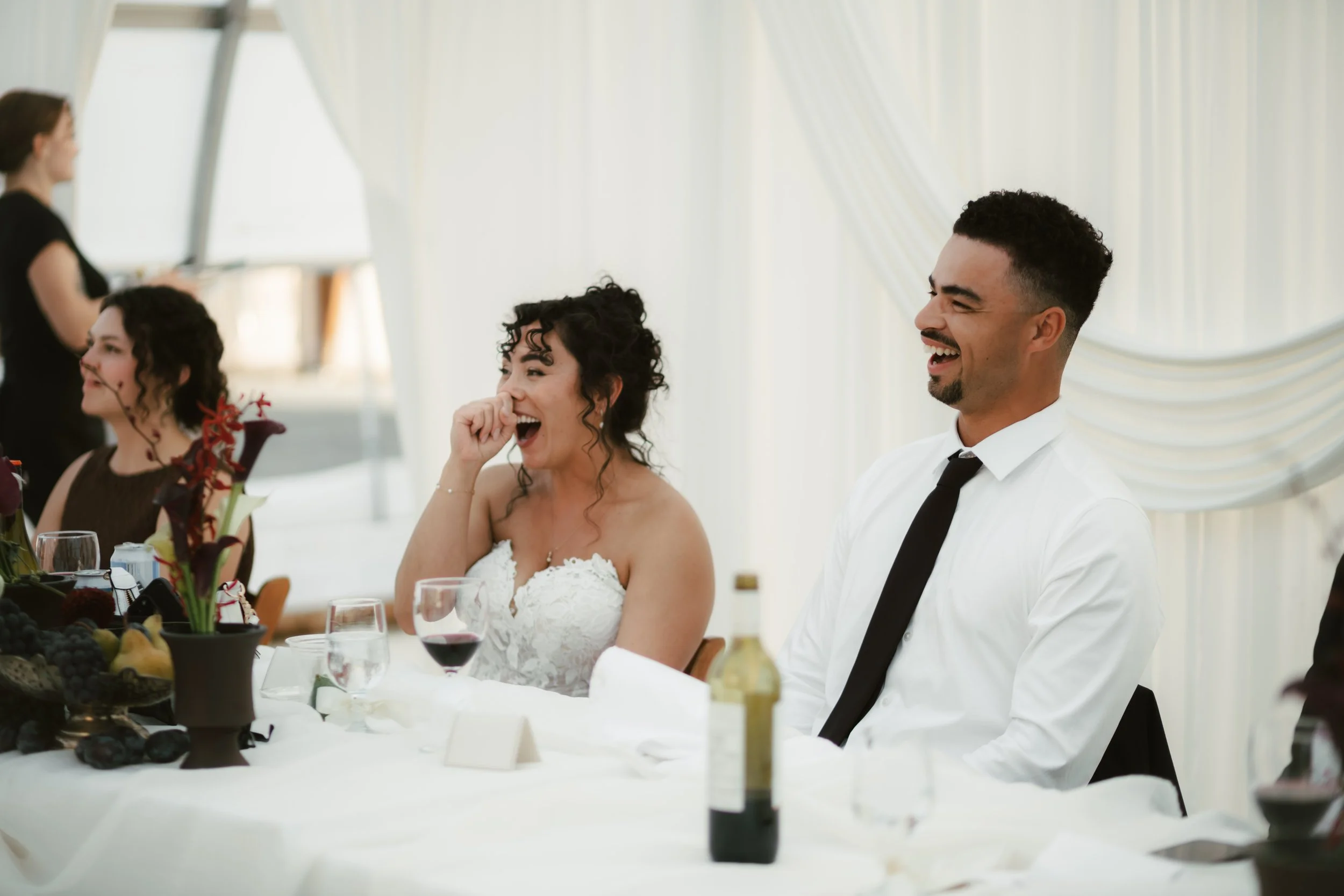Bride and groom laughing with wedding guests at a reception dinner