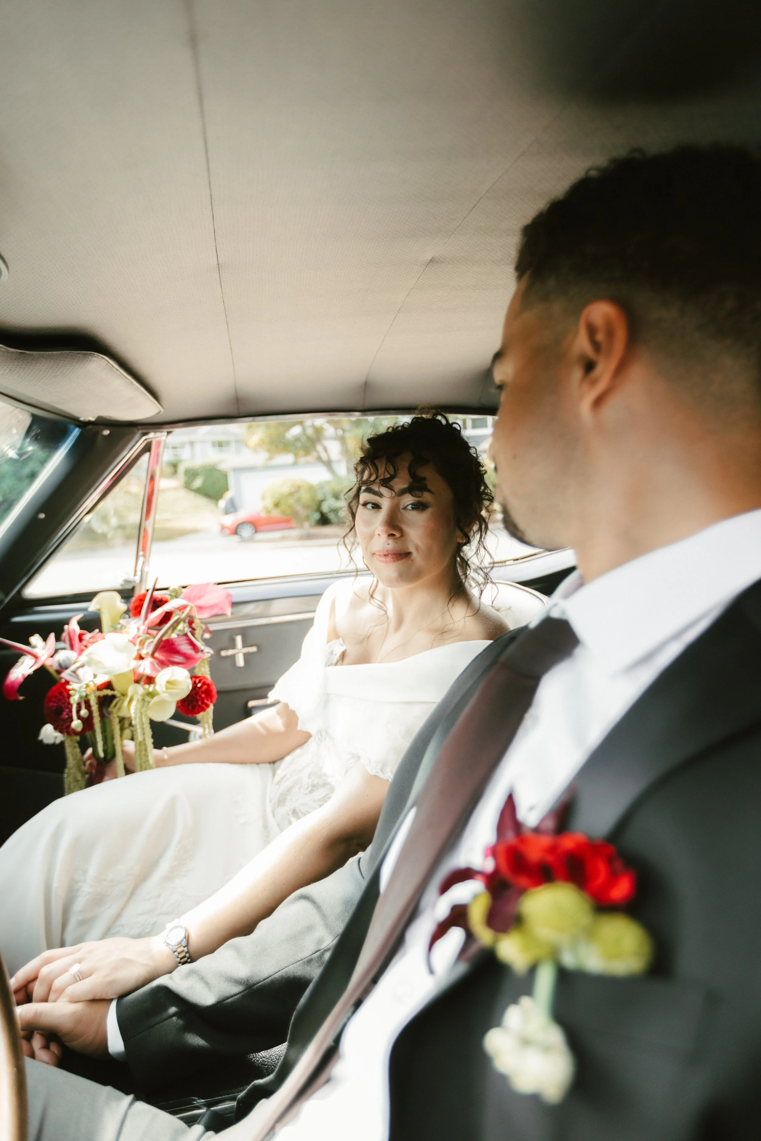 Bride and groom seated in a vintage car with wedding flowers