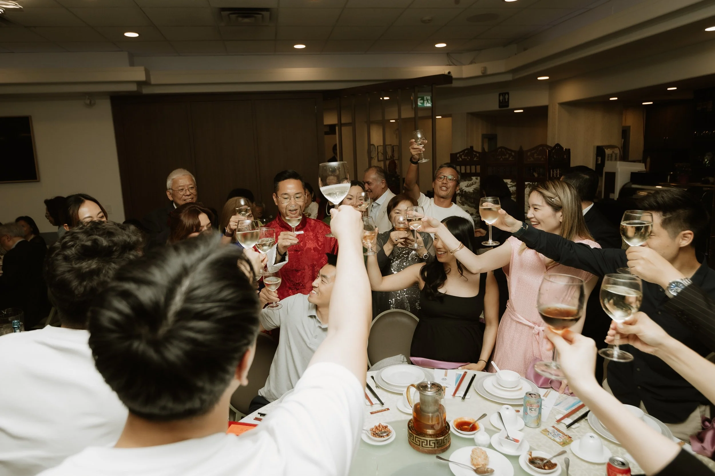 A diverse group of people celebrating at a dinner party, raising glasses of wine in a toast and smiling.