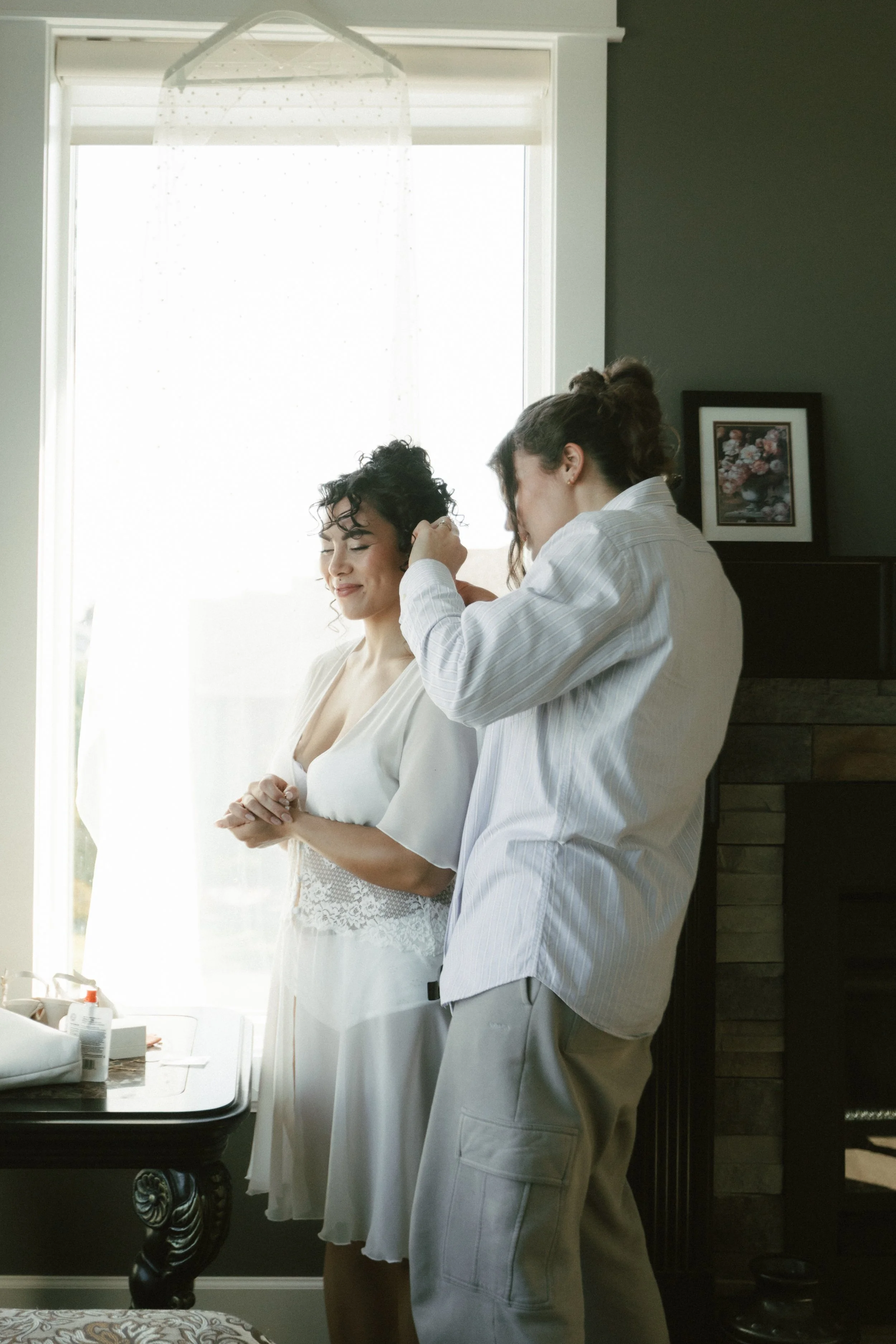 Woman styling another woman’s curly hair in a sunlit room
