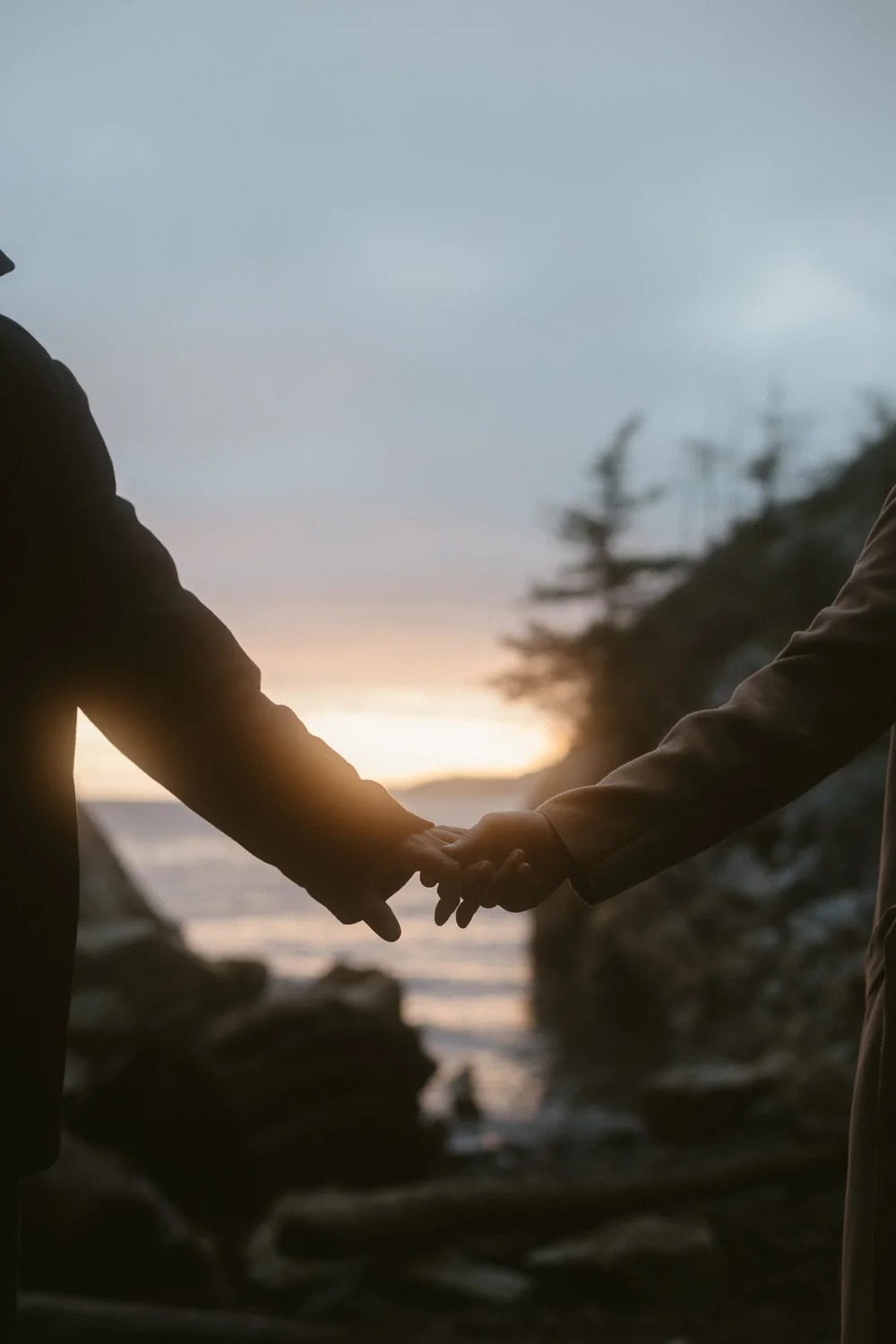 A couple holding hands at sunset on a rocky West Coast shoreline