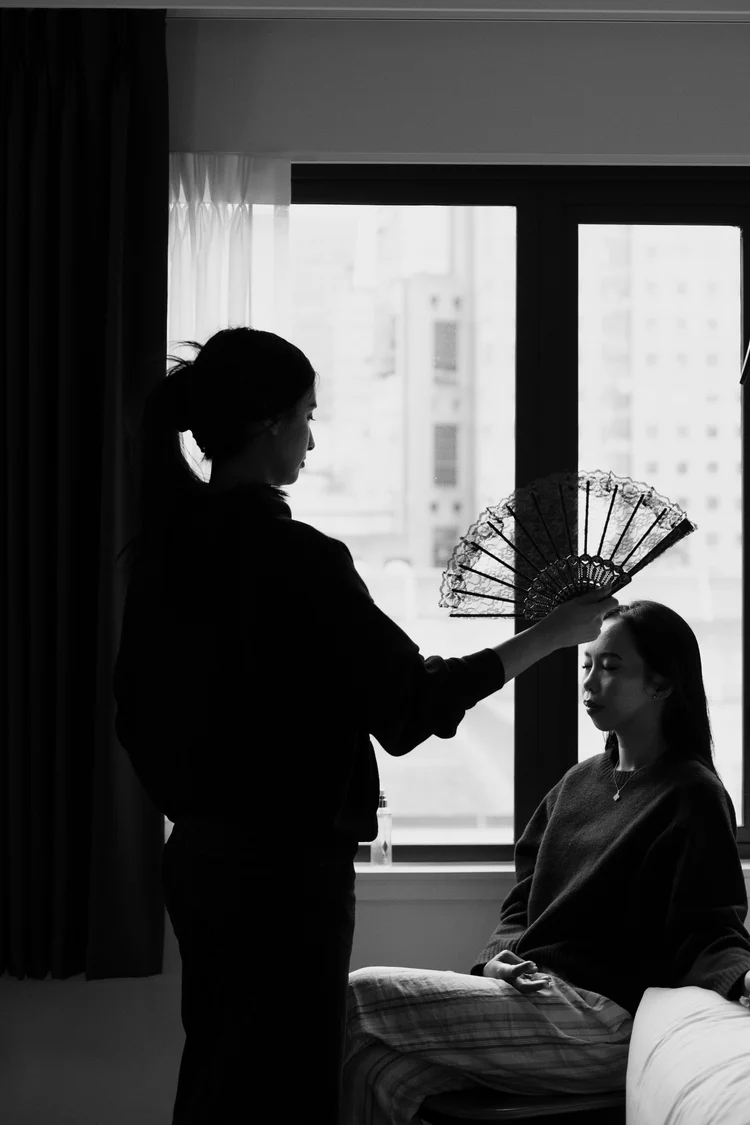Silhouettes by a bright window as a bride gets ready, a folding fan in hand