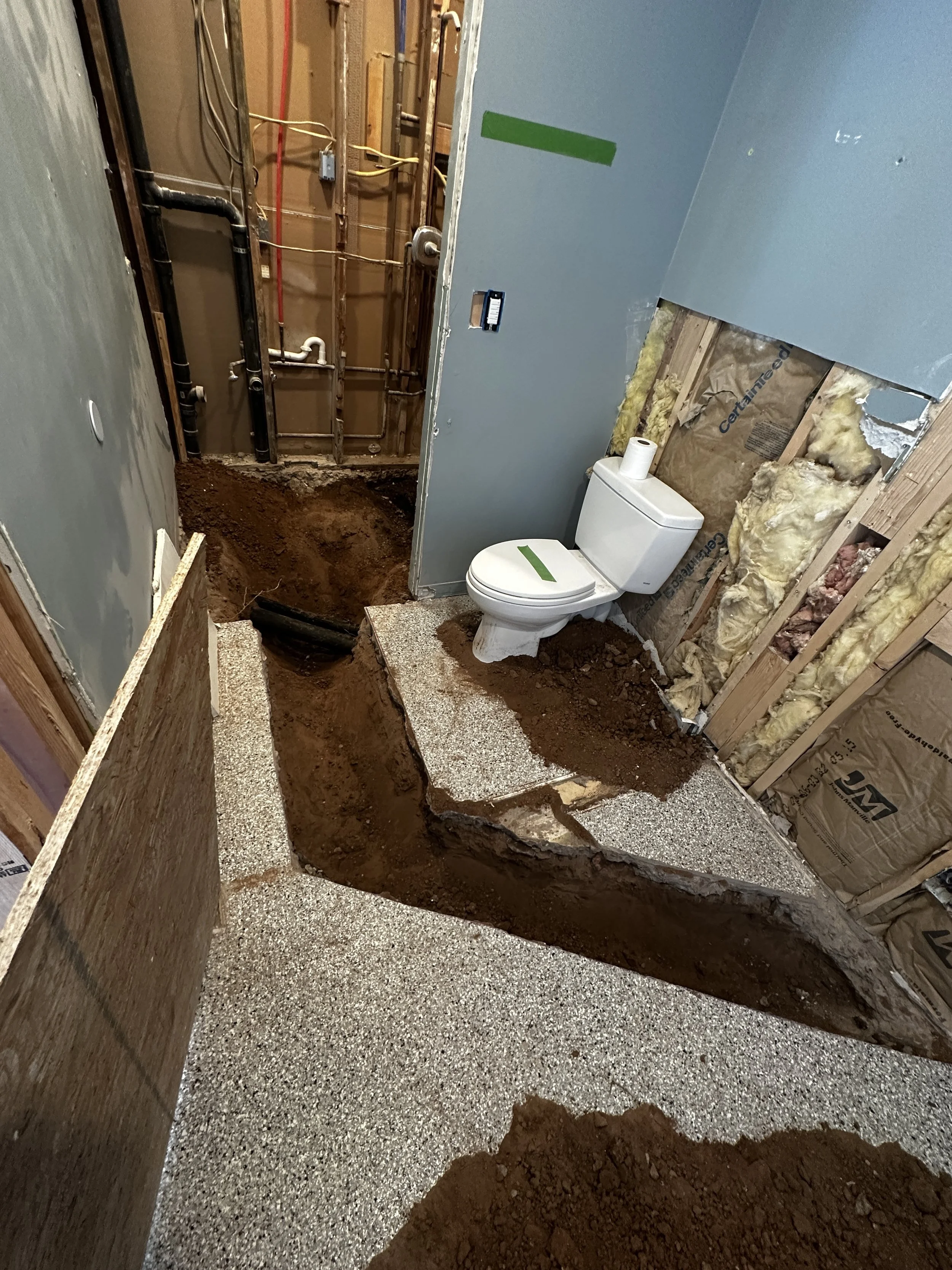 Bathroom under renovation with a toilet and exposed plumbing, dirt and debris on the floor, and insulation and drywall in progress.