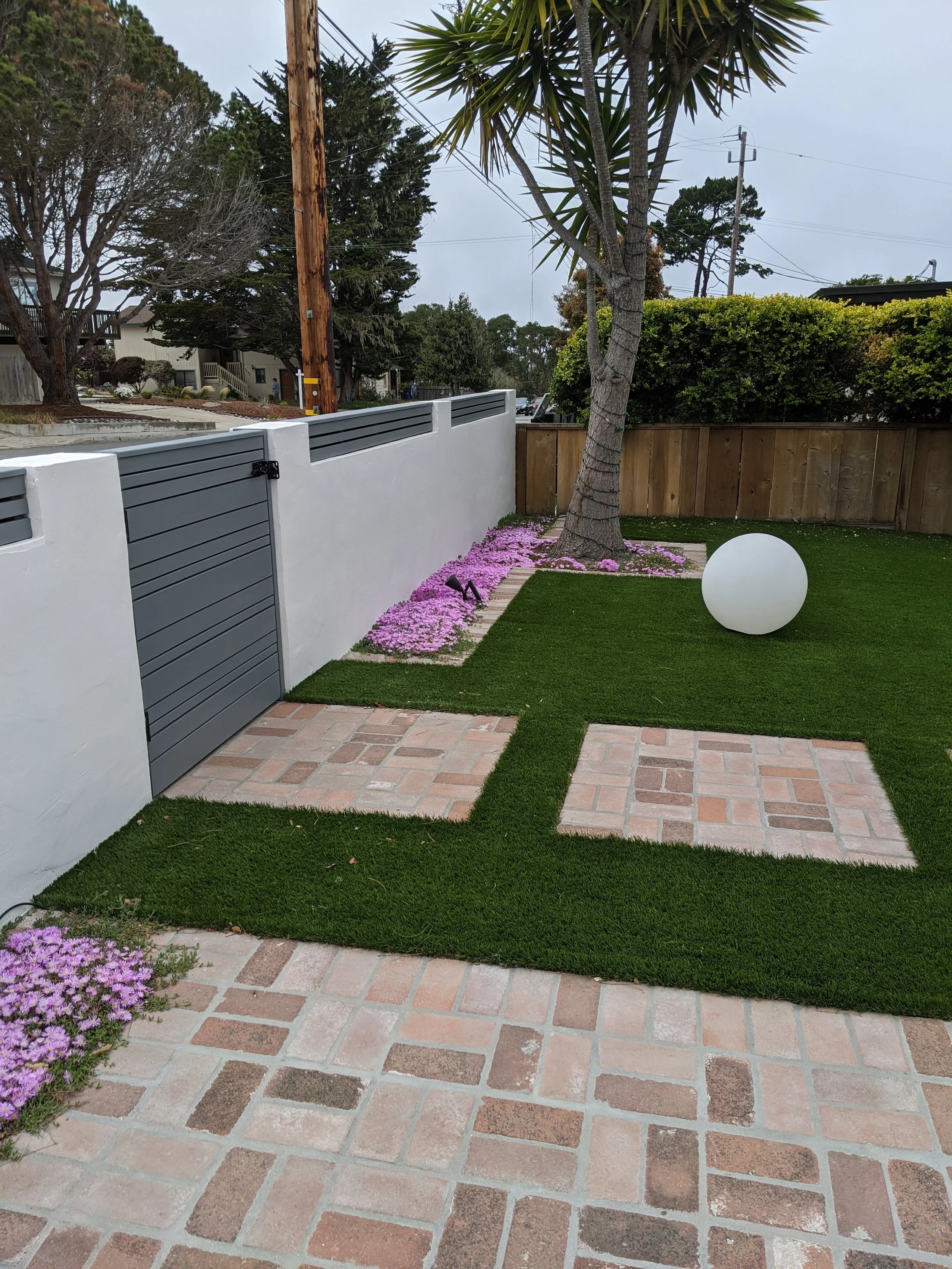 Clean front yard with artificial turf lawn for easy care and brick walkway. 