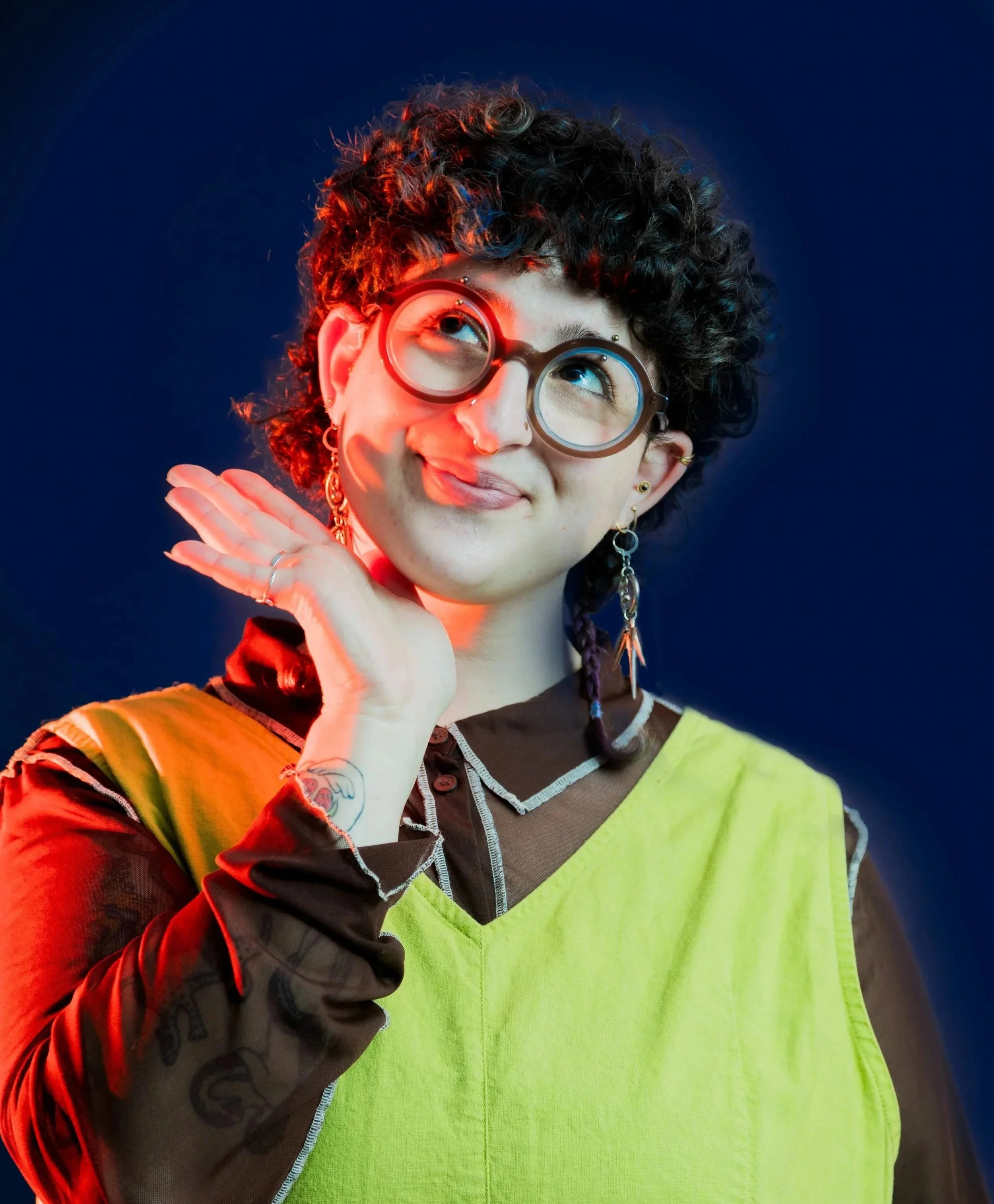 A smiling human, with their hand beneath their chin, portraying a warm and comforting environment, wearing a green and brown top.