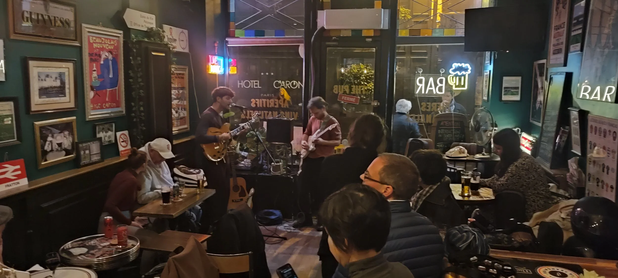Live music performance at a cozy pub with people sitting at tables and playing guitars.