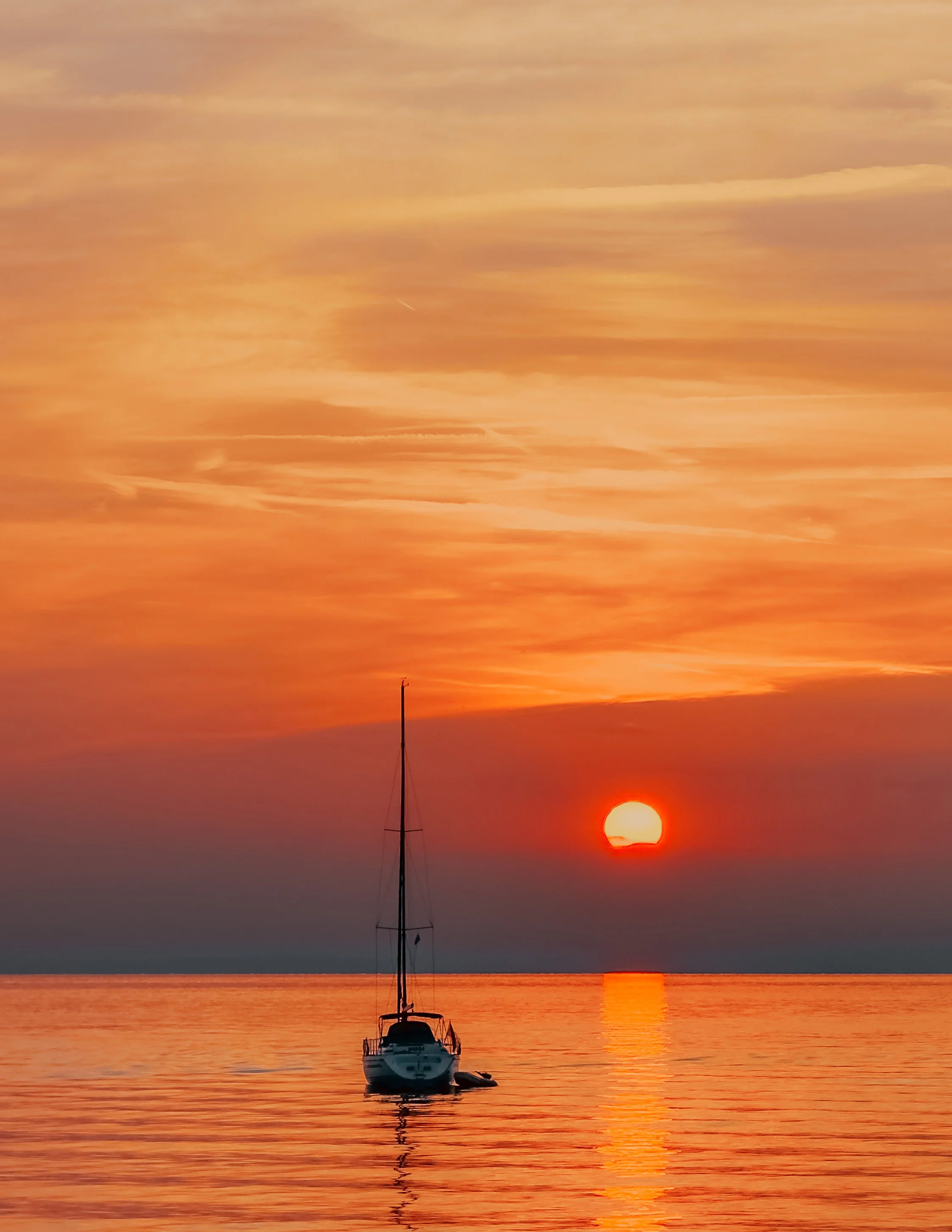 Sunset over calm water with a sailboat anchored in the foreground.