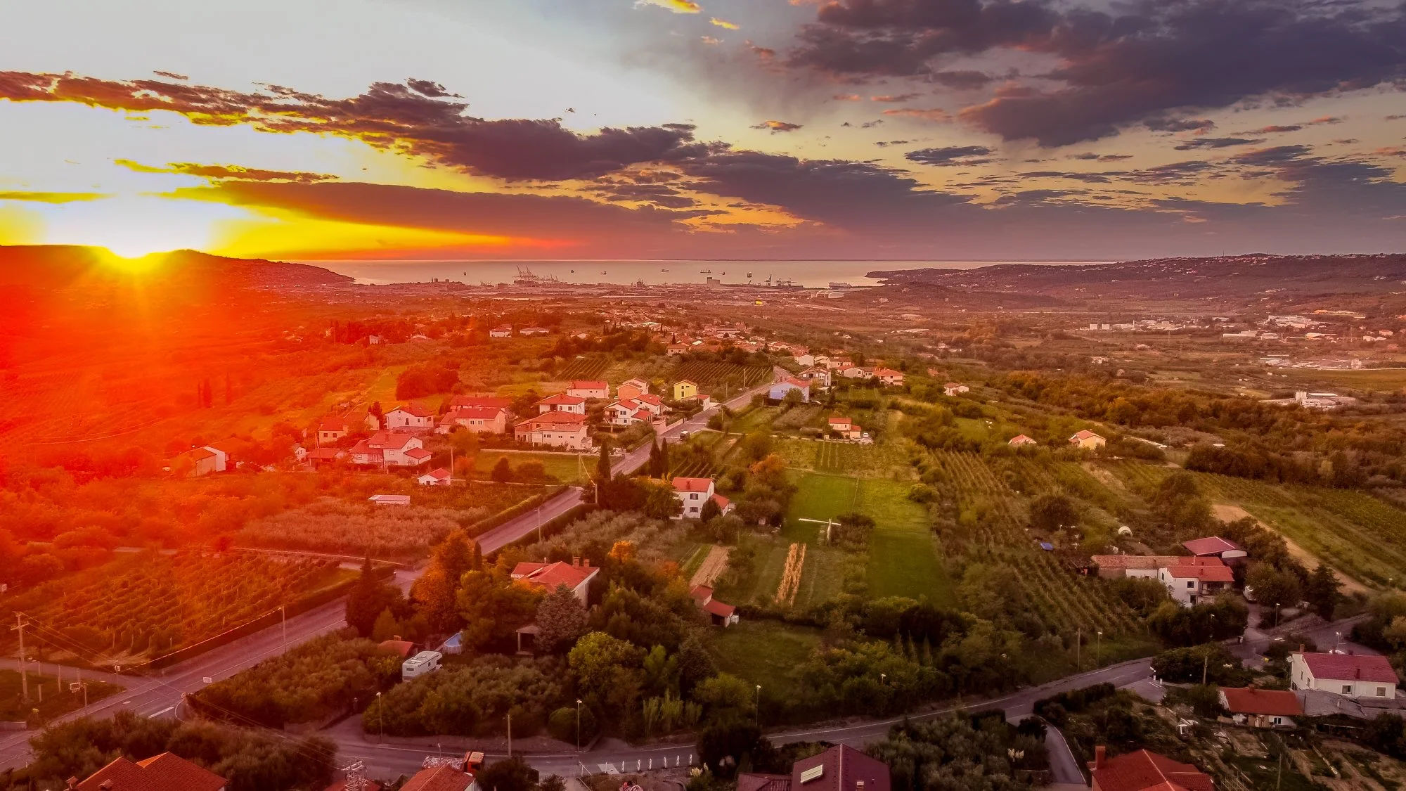 Sunset over a rural landscape with houses, vineyards, and a distant harbor with ships. Photo: Natali Gak.