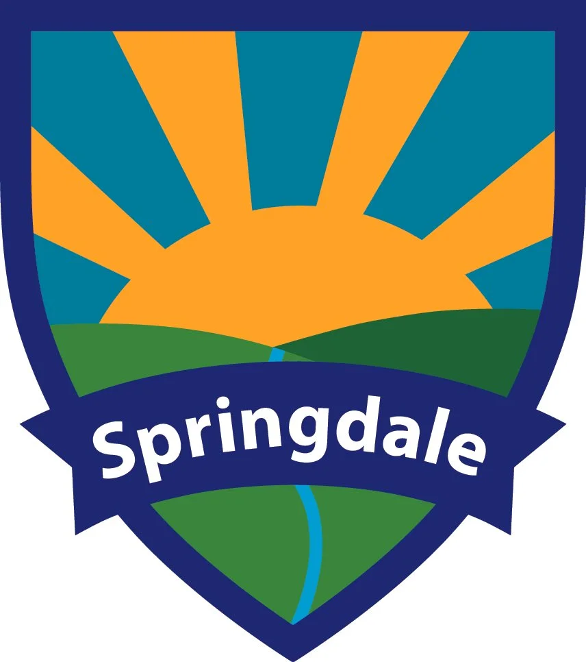 A shield-shaped logo featuring a stylized sunrise over green hills and a blue sky. The word 'Springdale' is written across the lower part of the shield.