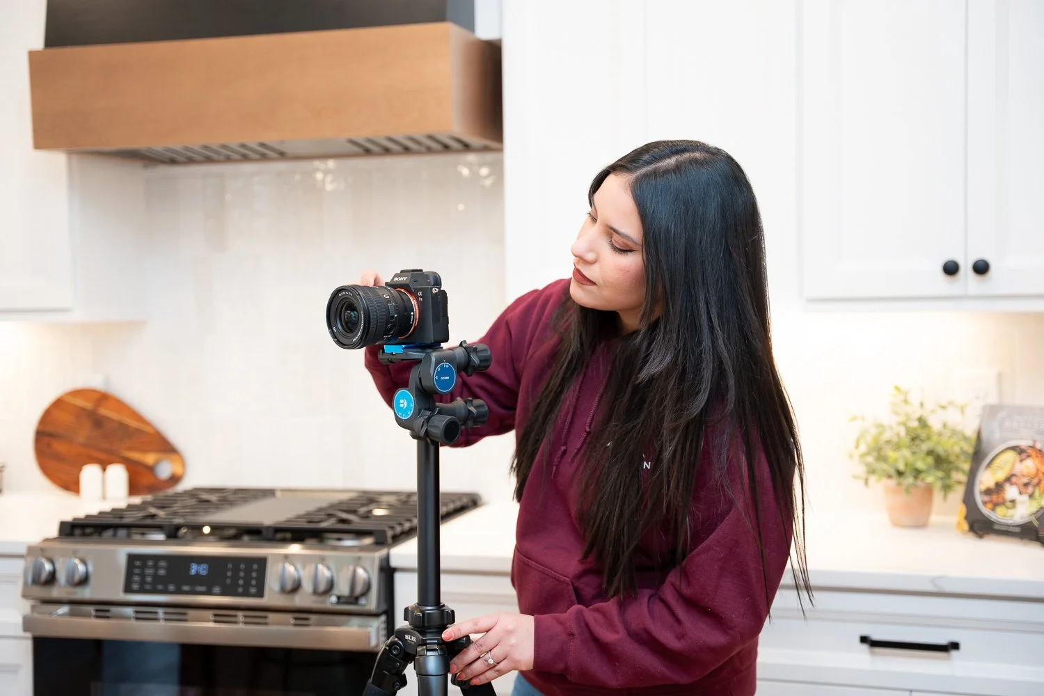 Woman adjusting a camera on a tripod in a kitchen.