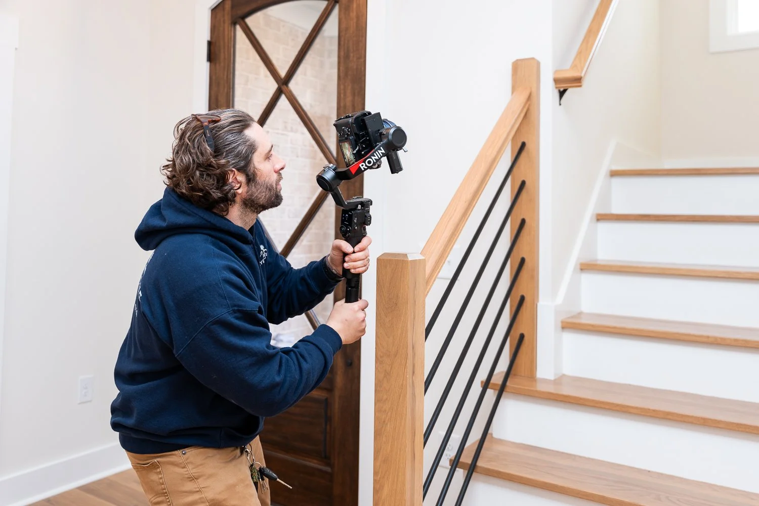 Man filming with a handheld camera stabilizer on staircase landing in a home.