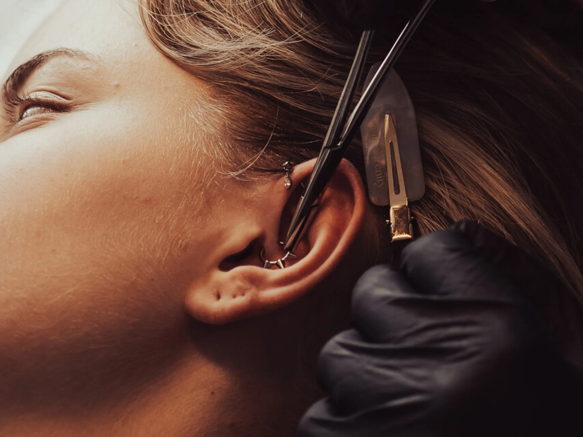 Ear Piercer downsizing posts of flat back labrets of clients piercings.