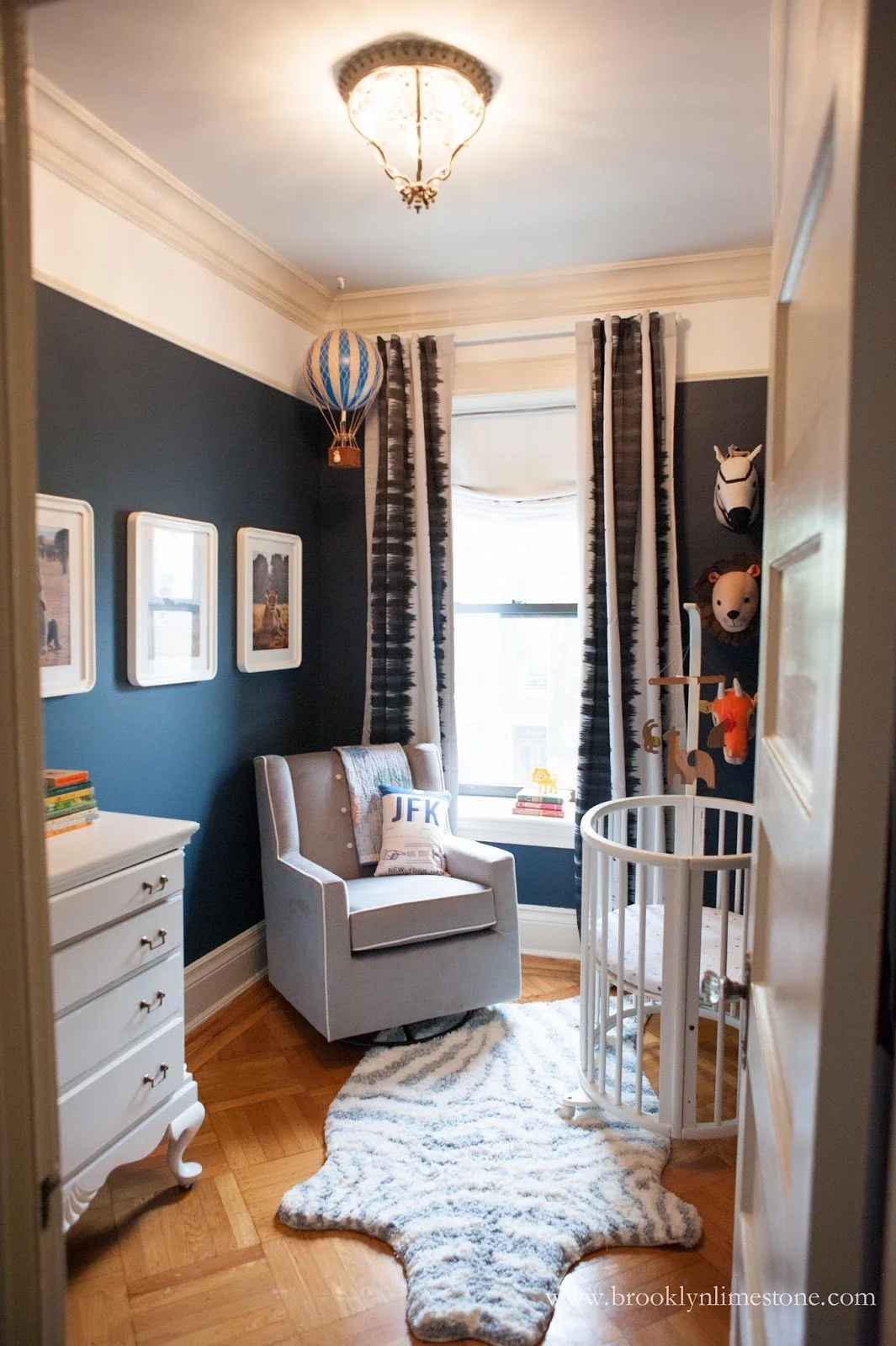 Cozy modern nursery with blue walls, gray chair, crib, hot air balloon decor, and animal wall art.