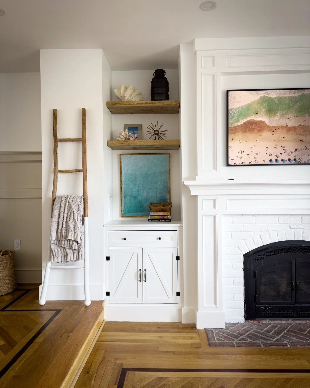 Stylish living room corner with white fireplace, ladder with blanket, wooden shelves with decor, and wall art.