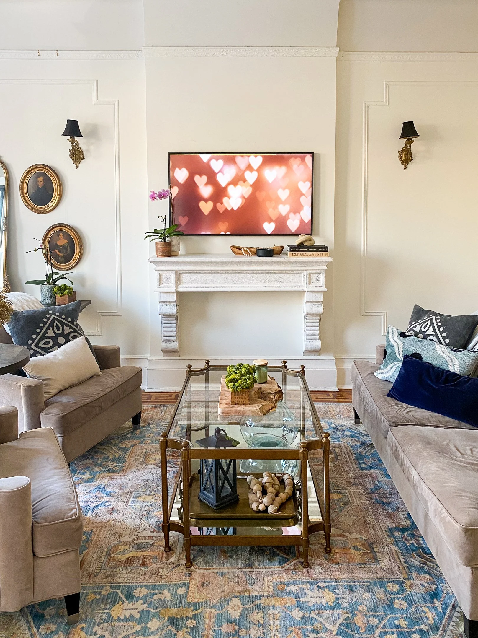 Elegant living room with two sofas, glass coffee table, decorative items, wall-mounted TV displaying heart shapes, and framed portraits on walls.