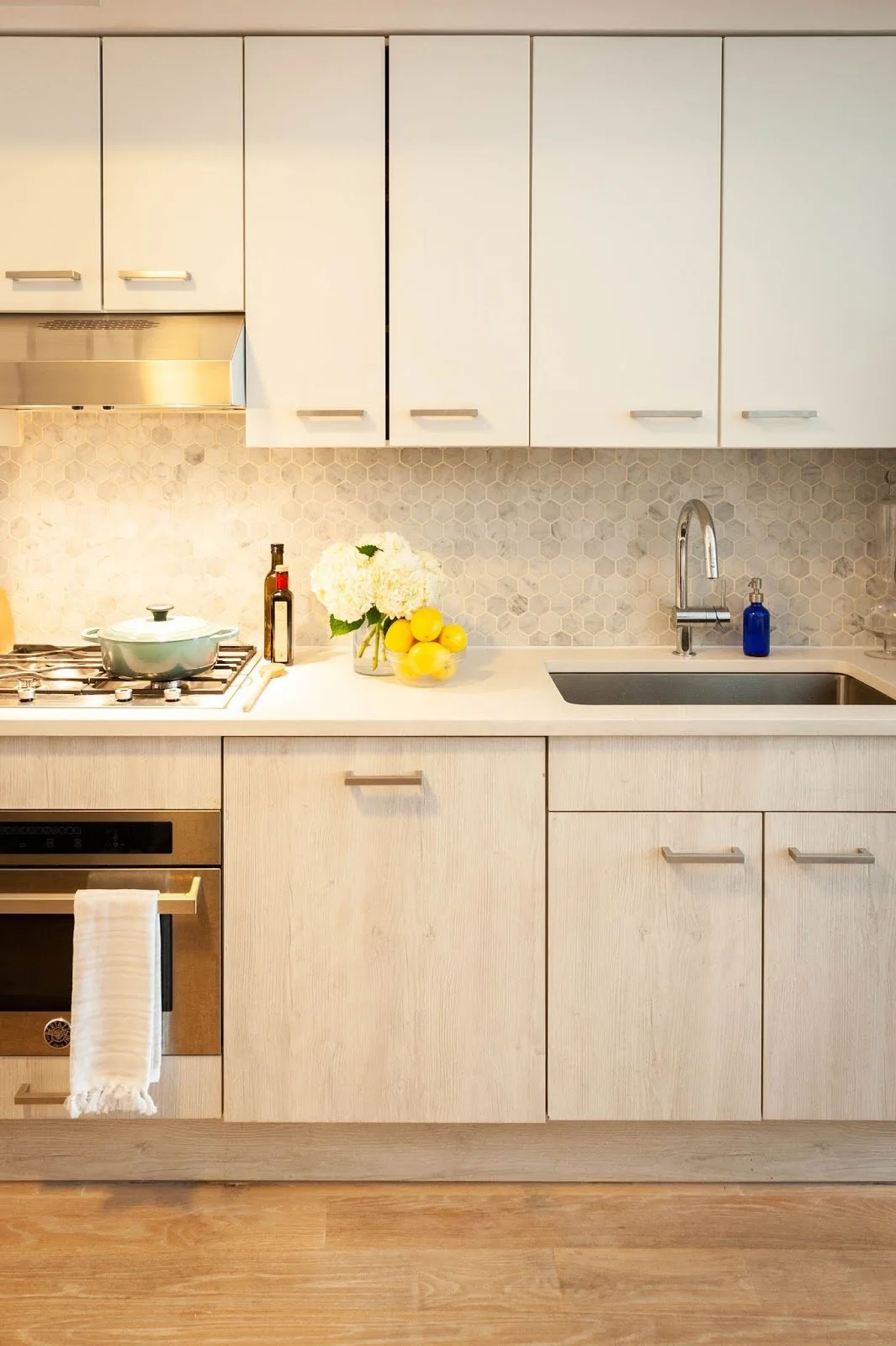 Modern kitchen with light wood cabinets, white countertops, gas stove, flowers, lemons, and kitchen sink.