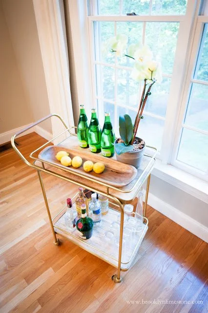 Elegant bar cart with lemons, green glass bottles, and potted orchid.