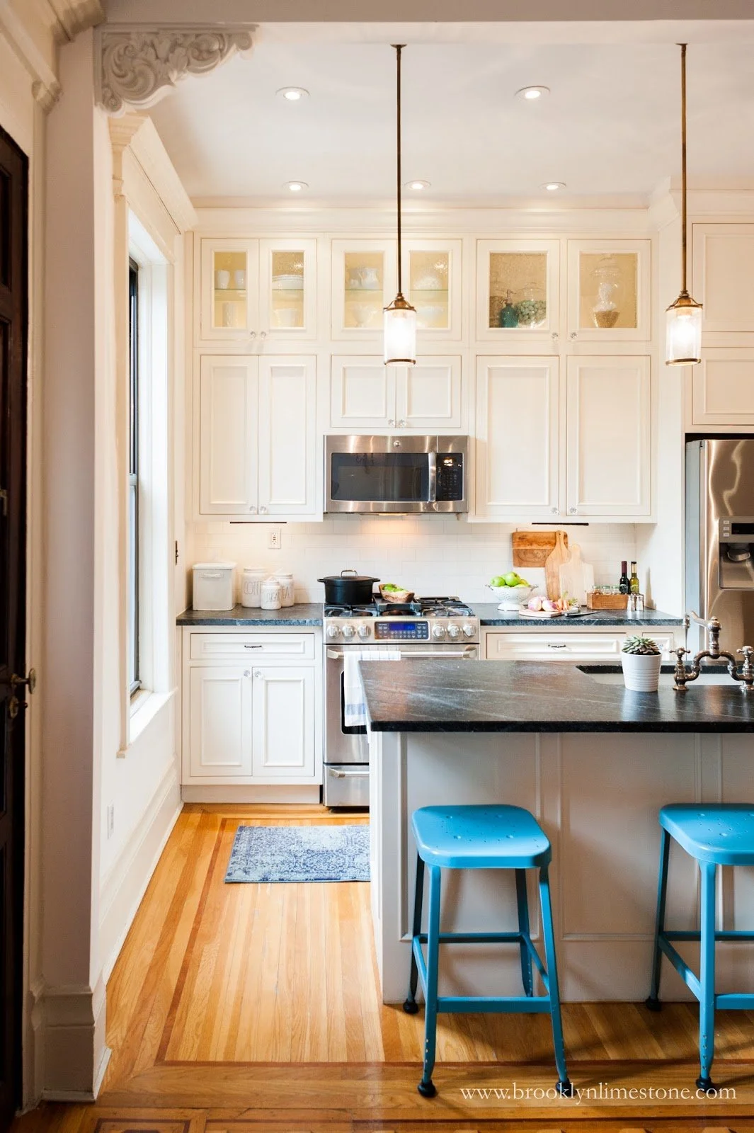 Modern kitchen with white cabinets, stainless steel appliances, black countertop island, and blue stools.