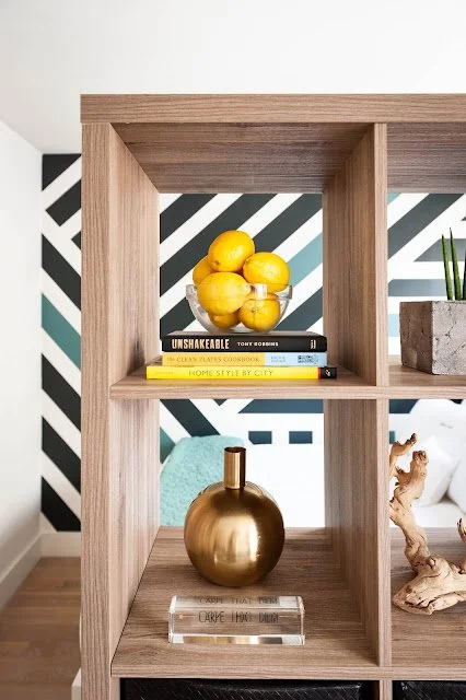 Wooden bookshelf with books, lemons, golden vase, abstract art background