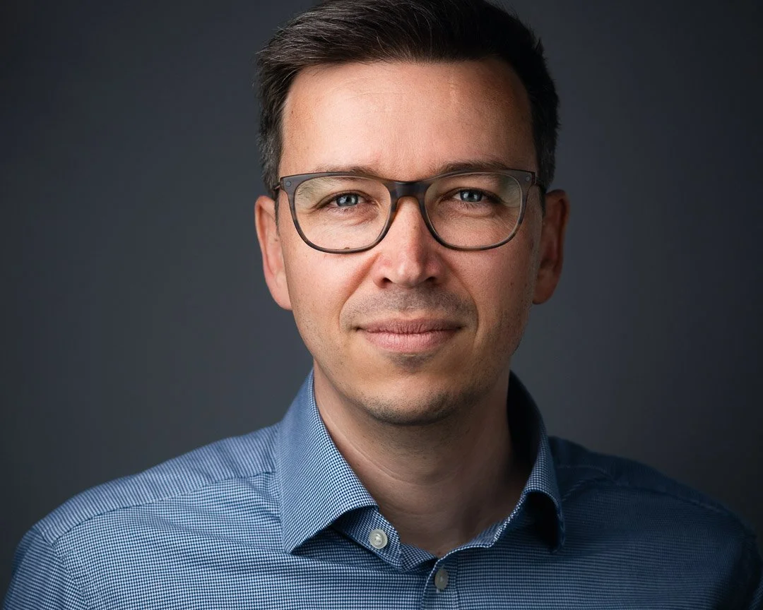 Profilbild für Linkedin eines Mann mit dunklen Haaren, Brille und blauem Hemd