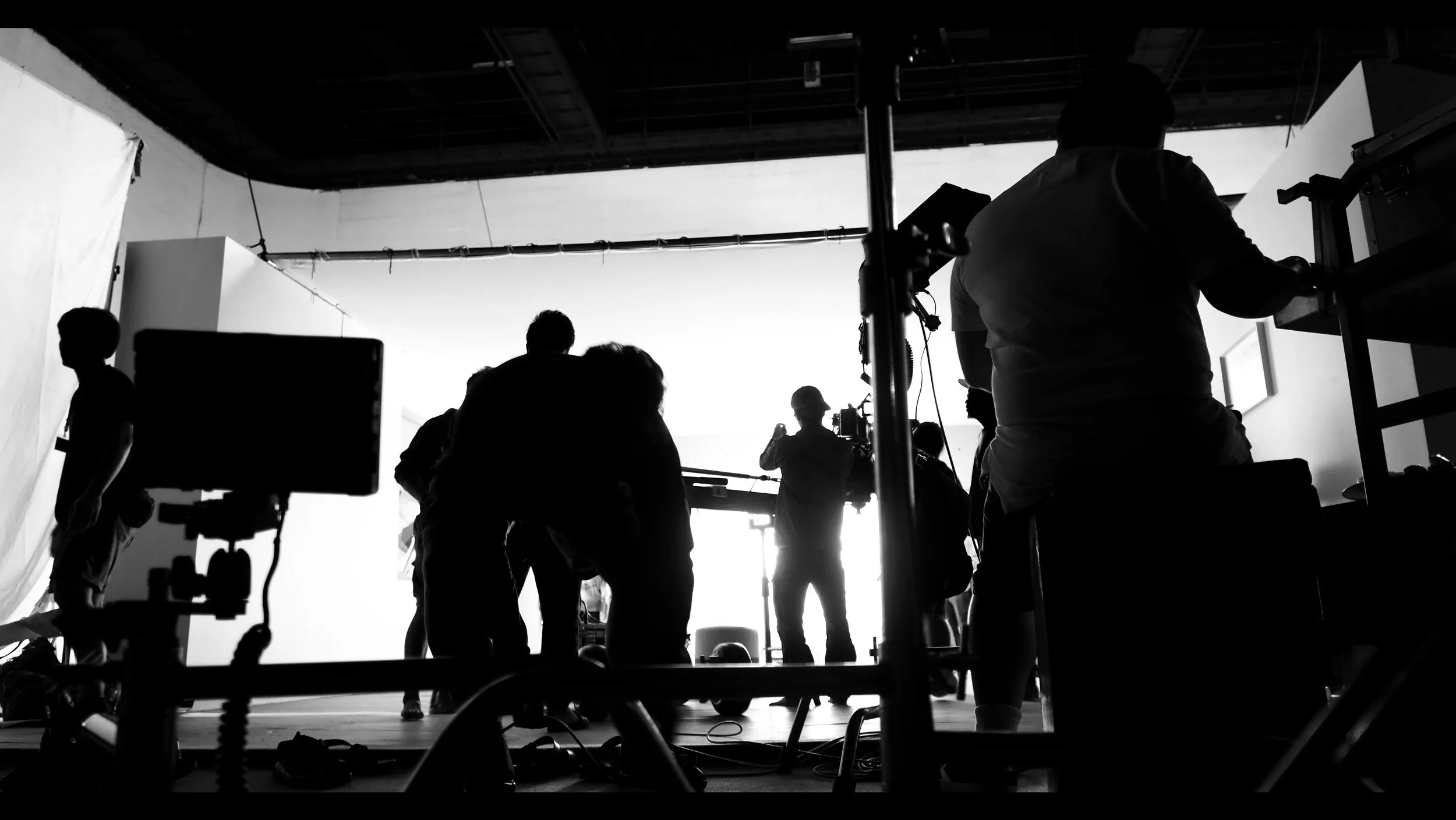 Silhouettes of people on a film set or photography studio, with equipment and a bright background.