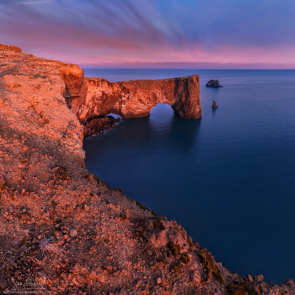 ramatic sunset panorama titled "Burning Bay" at Dyrhólaey, Iceland. Black sand beach and sea stacks illuminated by intense red and orange sky. Captured by Jan Smid, Master QEP, during a 2015 photo expedition. Fine art landscape.