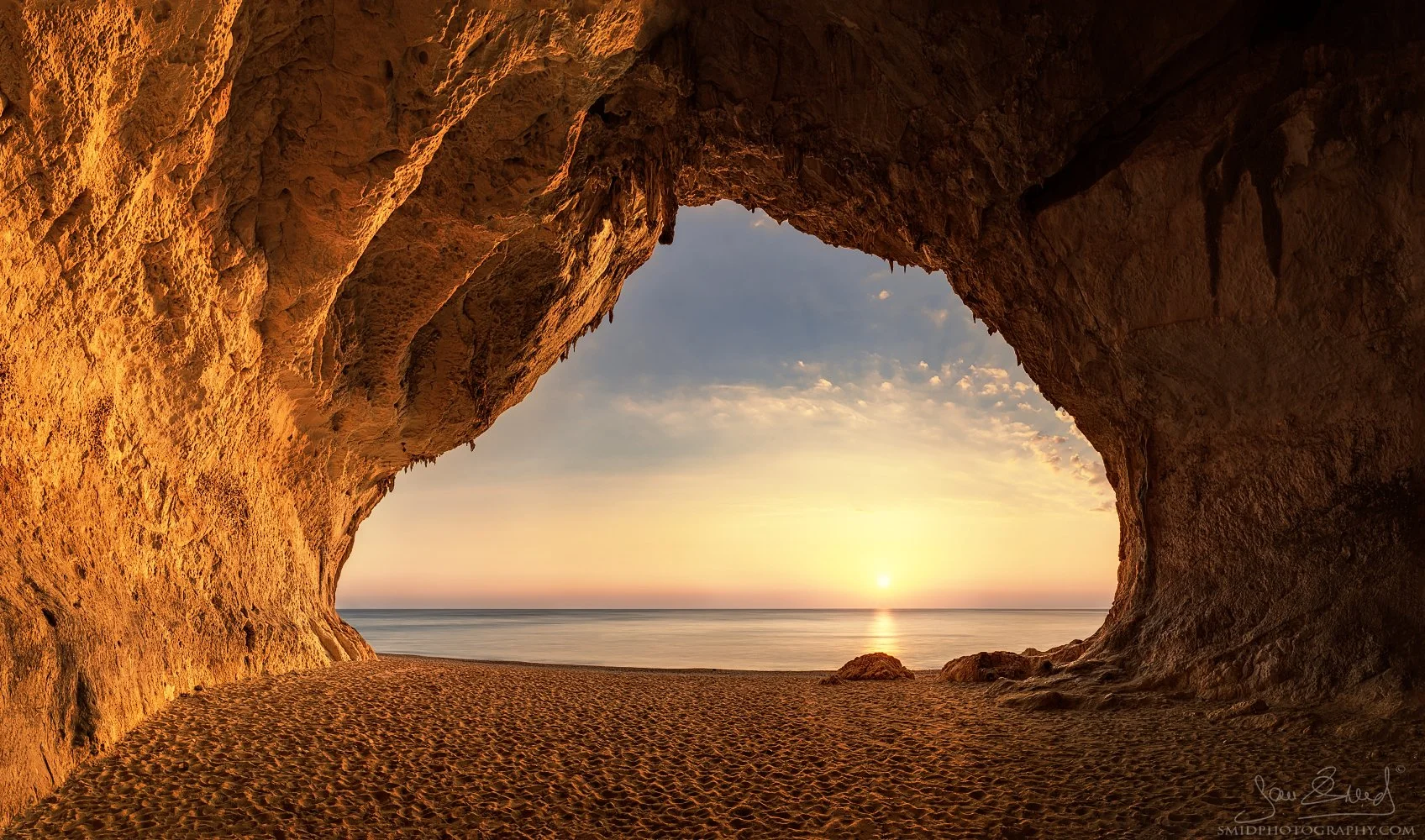Spectacular sunrise viewed from inside a giant sea cave at Cala Luna beach, Sardinia. Captured by Jan Smid, Master QEP, during a 2020 photography expedition. Golden morning light illuminating the cave interior and Mediterranean Sea.