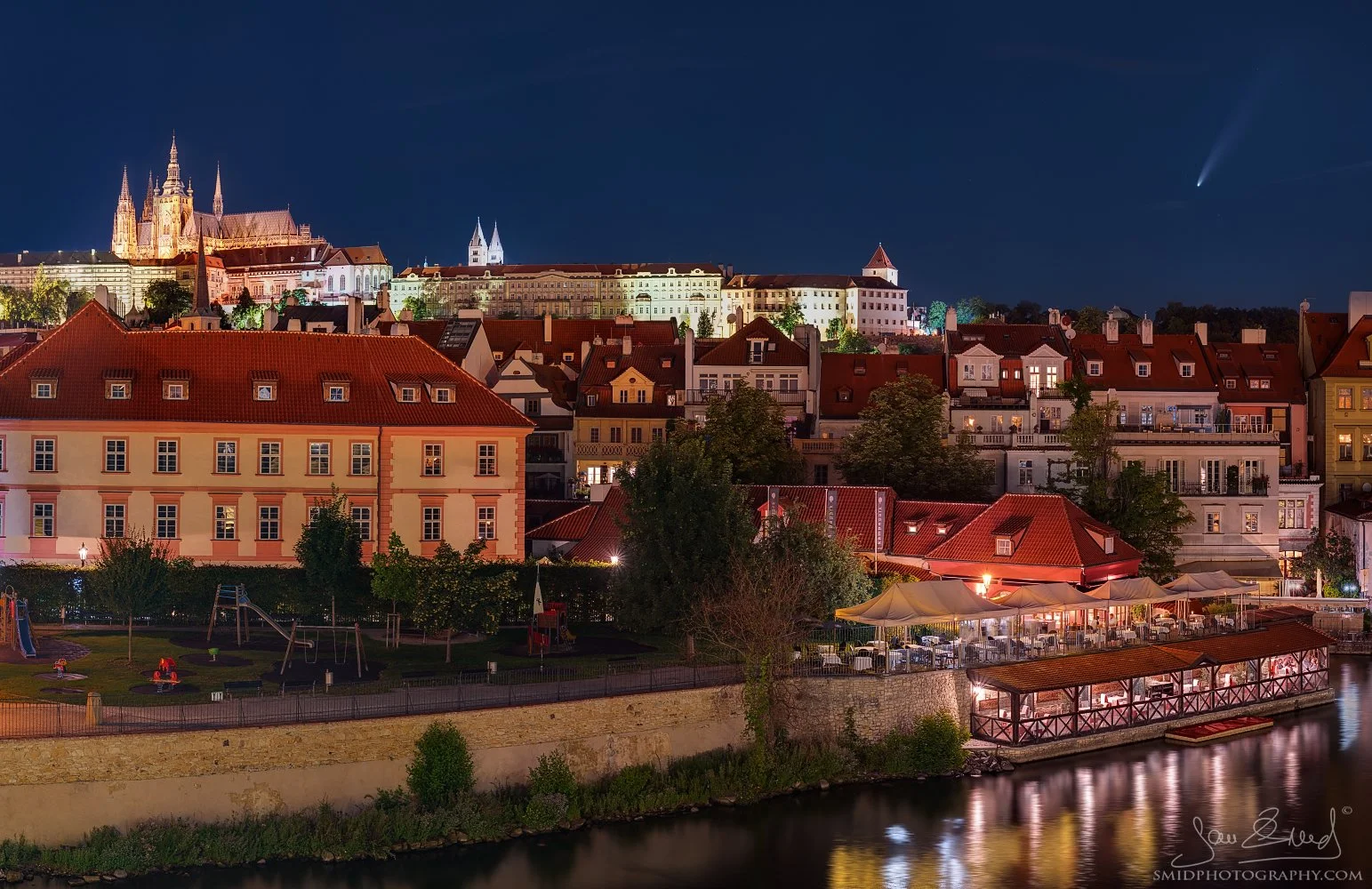Stunning astrophotography titled "The Comet Neowise above Prague." Comet C/2020 F3 (NEOWISE) with a visible tail shining over the illuminated Prague Castle and St. Vitus Cathedral. Captured by Jan Smid, Master QEP, in 2020.