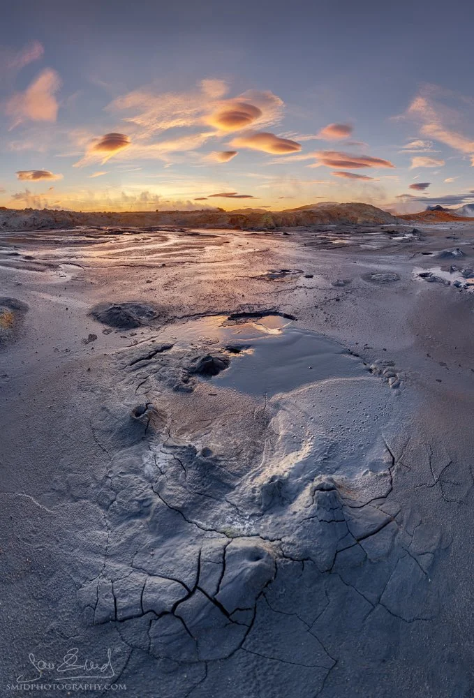 Wide-angle landscape of bubbling mud pots at Hverir, Iceland, captured during the Autumn 2025 expedition. Glowing orange clouds at sunrise over geothermal field textures. Master QEP photography.